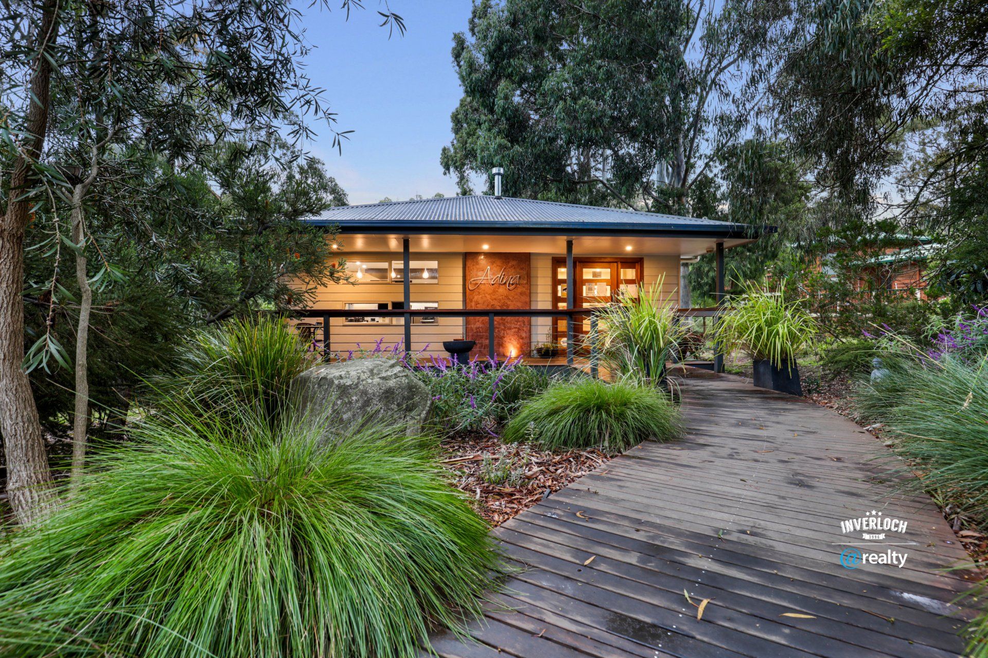 A small house is surrounded by trees and bushes and has a wooden walkway leading to it.
