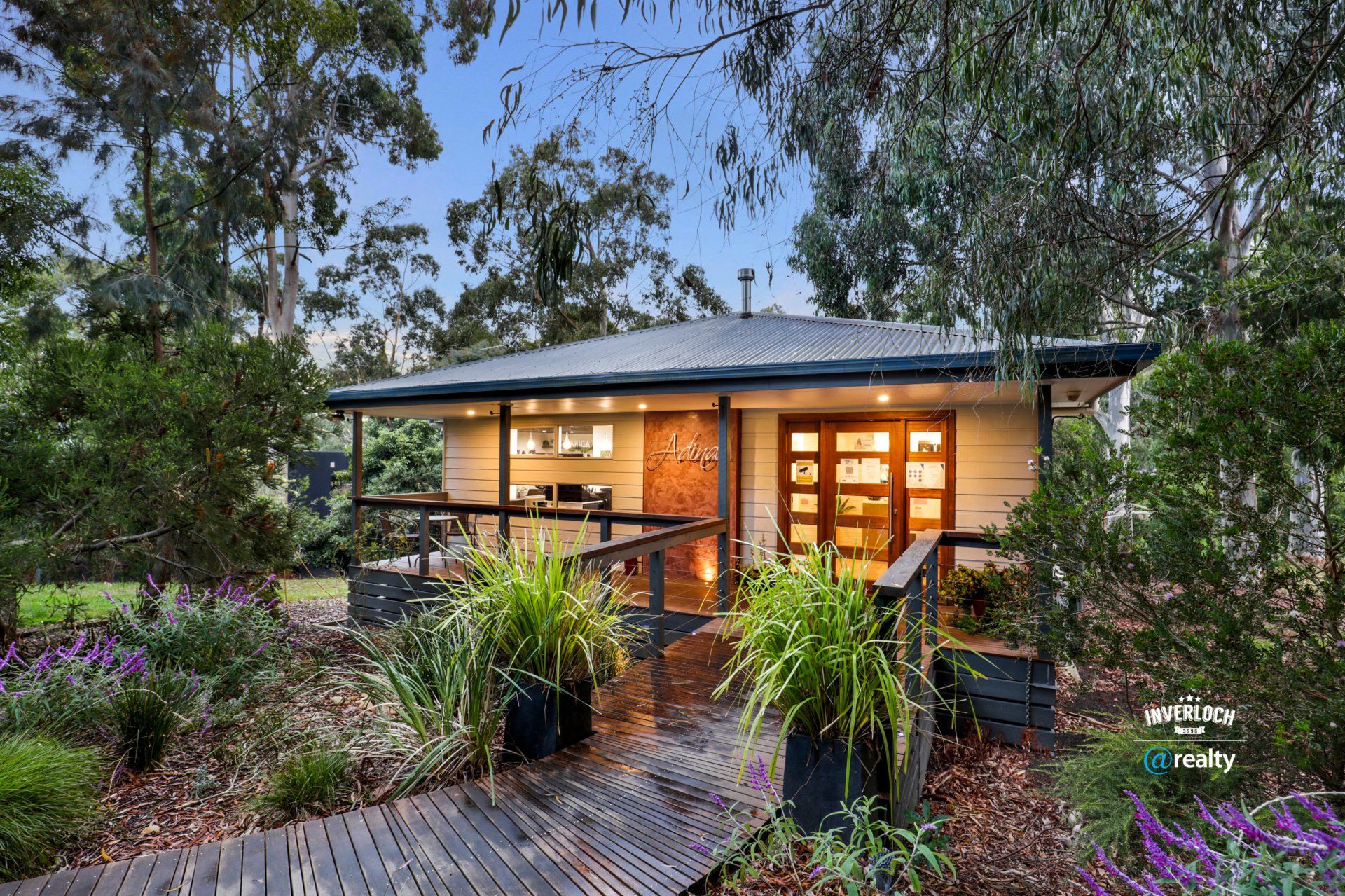 A small house with a wooden walkway leading to it is surrounded by trees.
