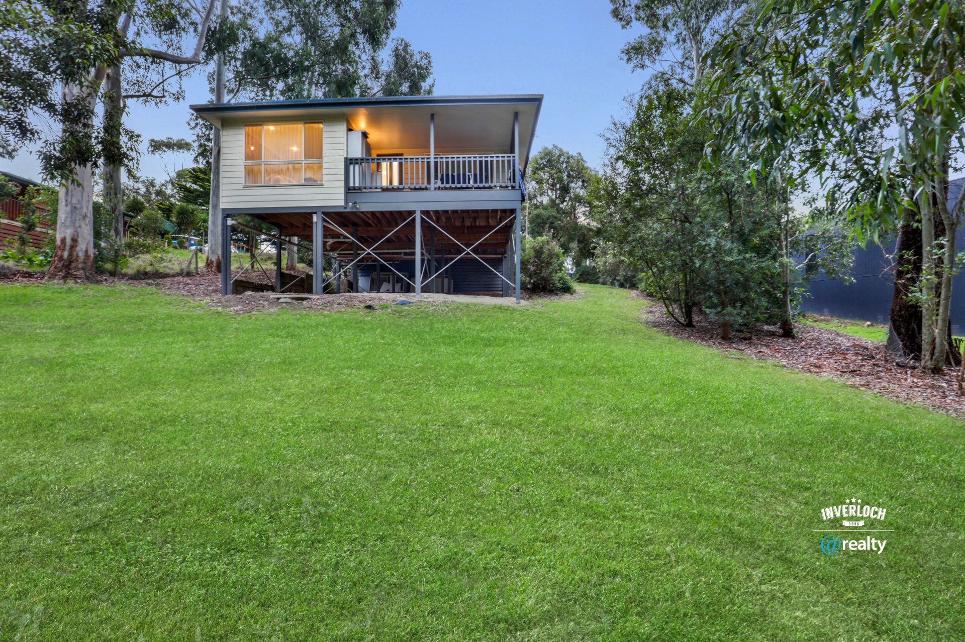 A house on stilts with a large lawn in front of it.