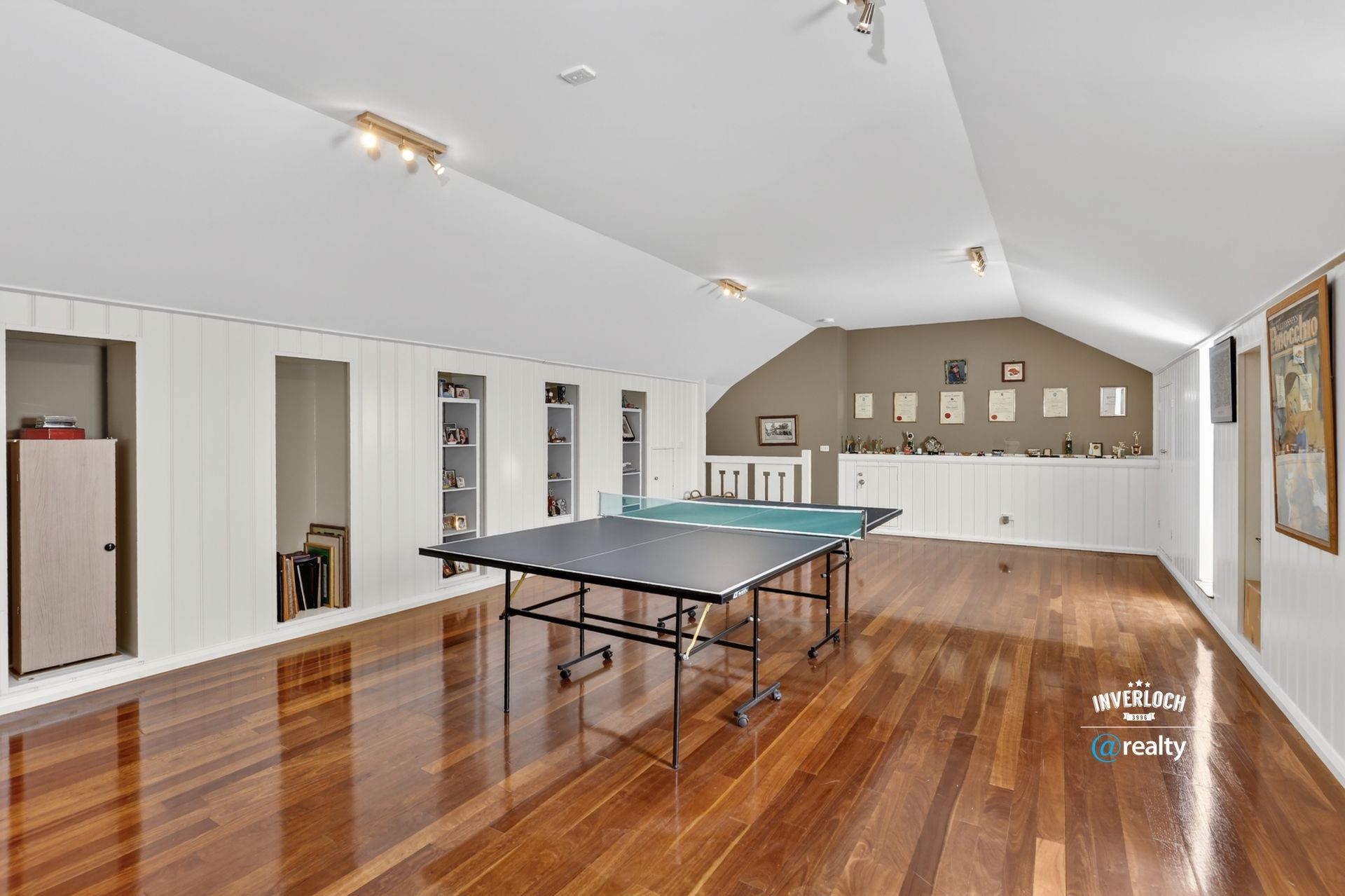 Spacious room with ping pong table, hardwood floors, white walls, and built-in storage.