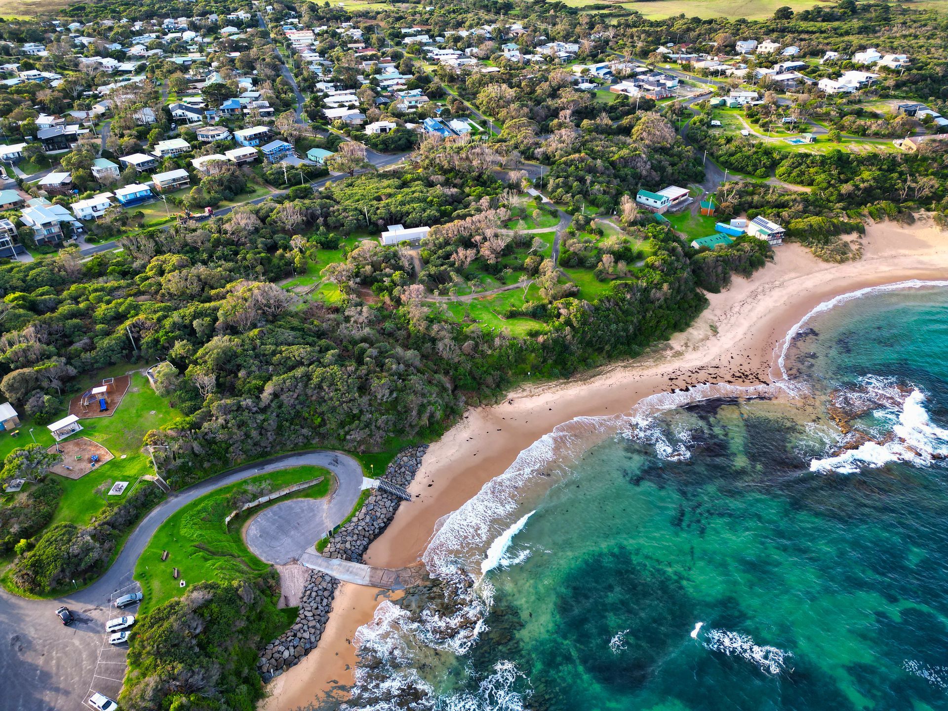 Aerial view of a tropical coastline with turquoise water, sandy beach, and lush green hillside homes