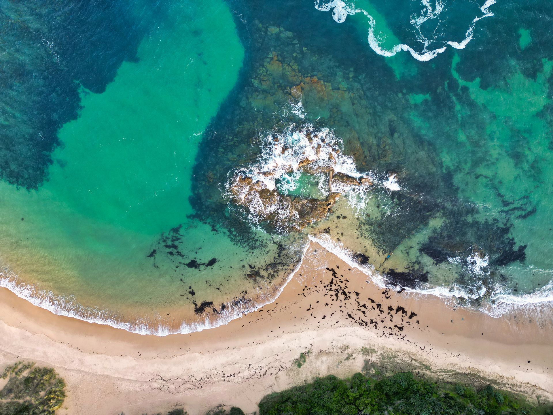 Aerial view of a turquoise shoreline with sandy beach, rocky outcrops, and waves breaking along the coast.