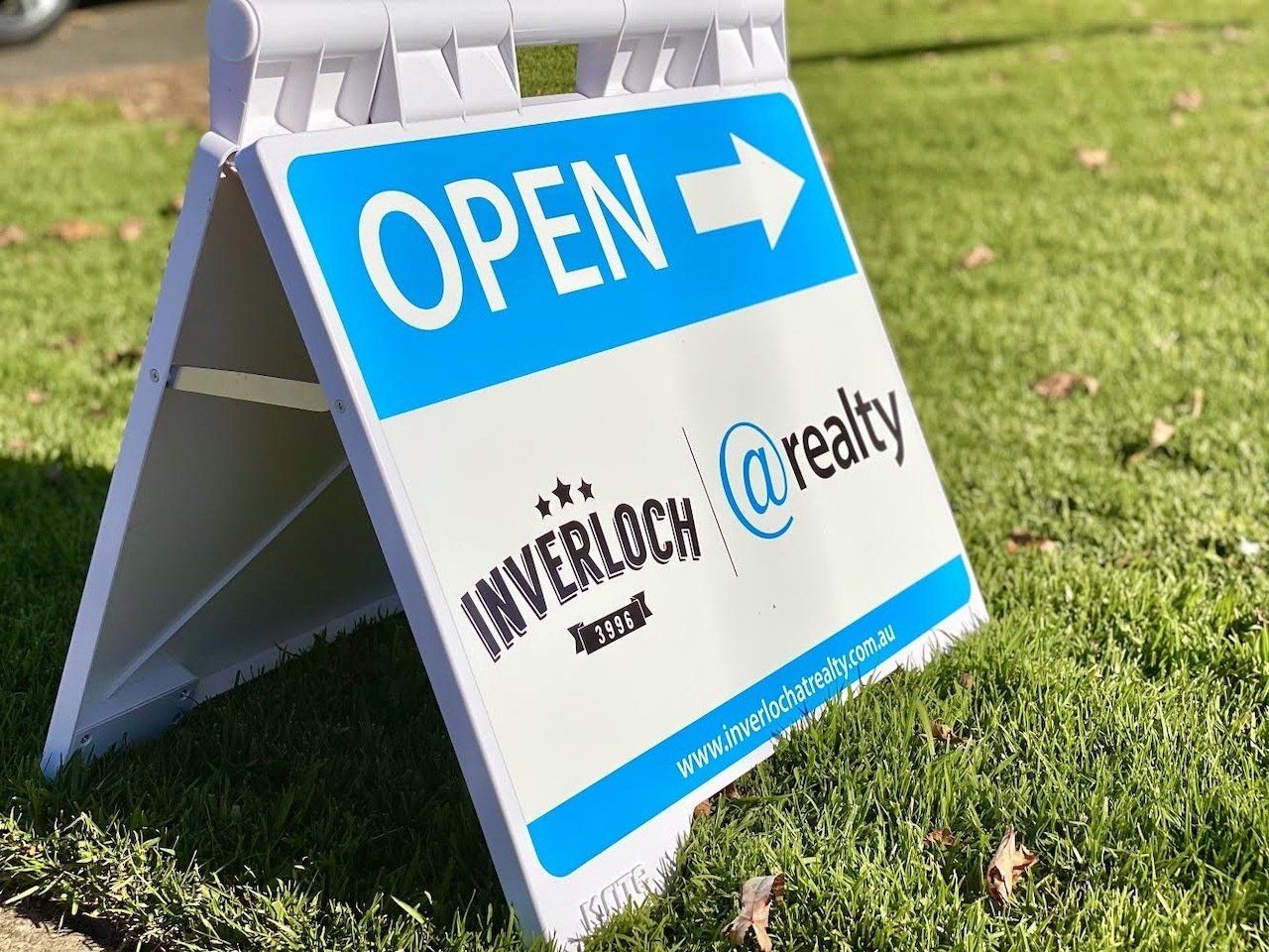 A blue and white sign that says open is sitting in the grass.