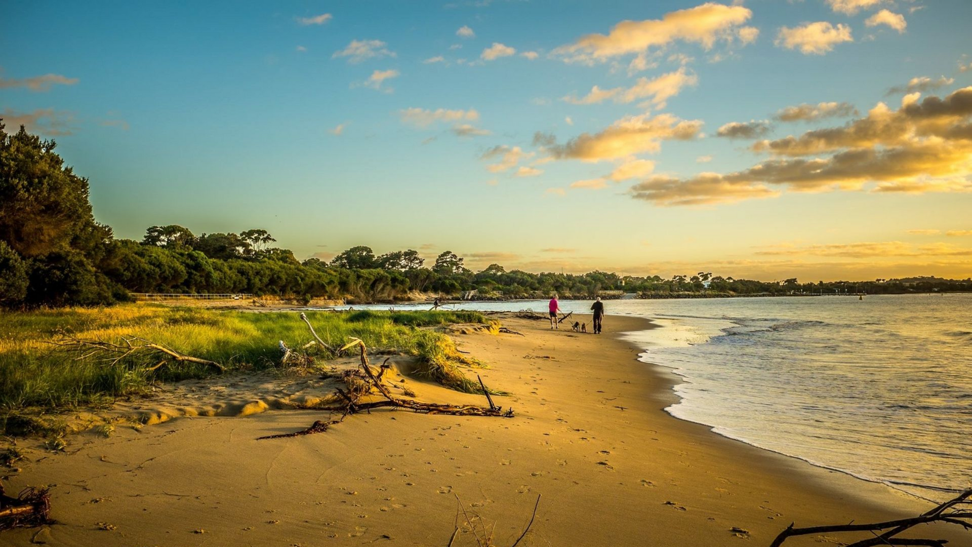 Sunny beach with gentle waves, golden sand, and two people near the shoreline at sunset