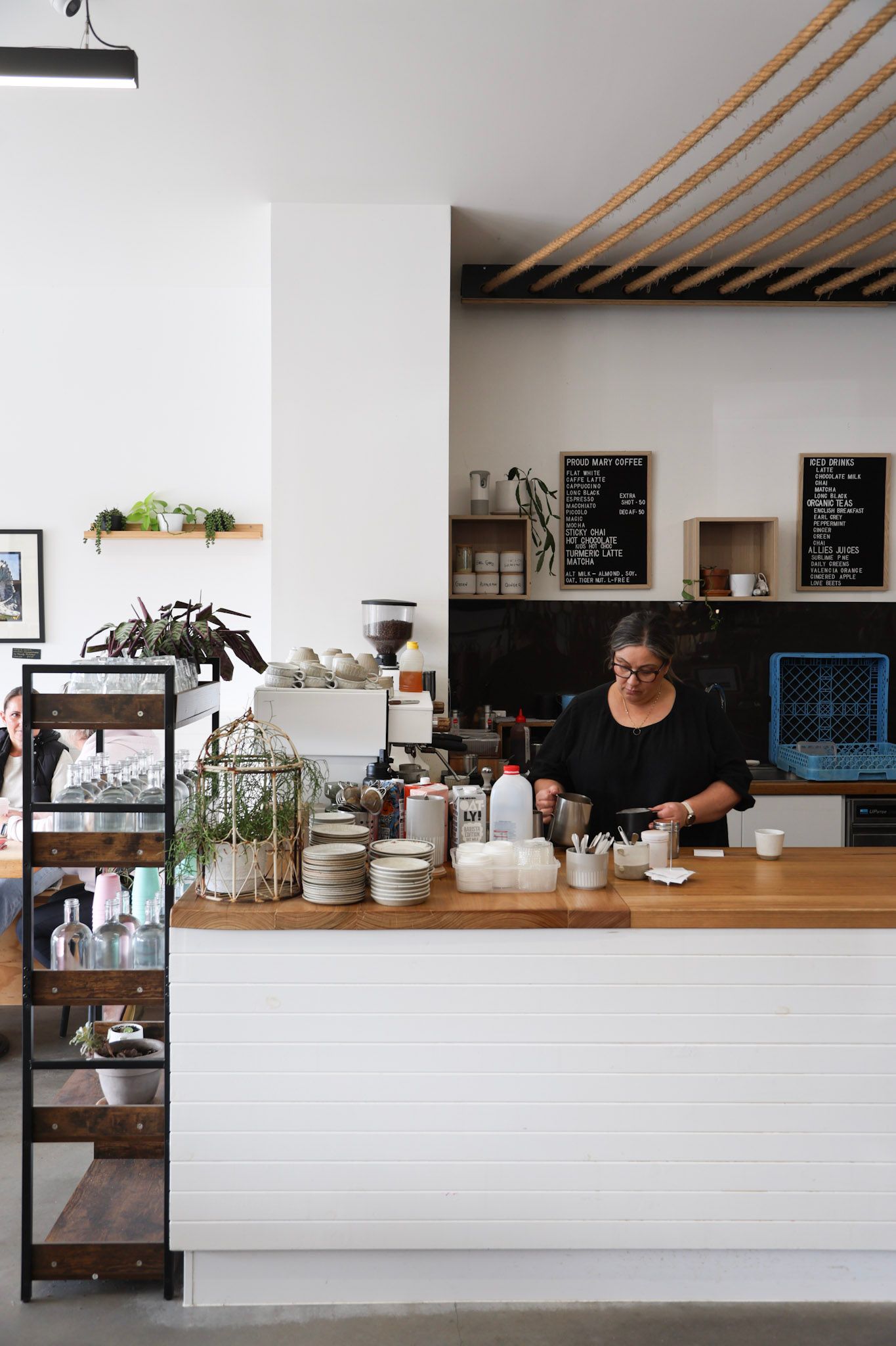 Barista behind wooden cafe counter with jars and cups in a bright modern coffee shop