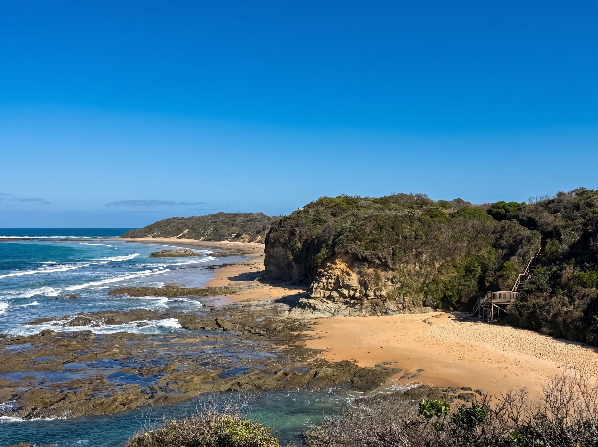 Rocky beach cove with turquoise water, sandy shore, and clear blue sky