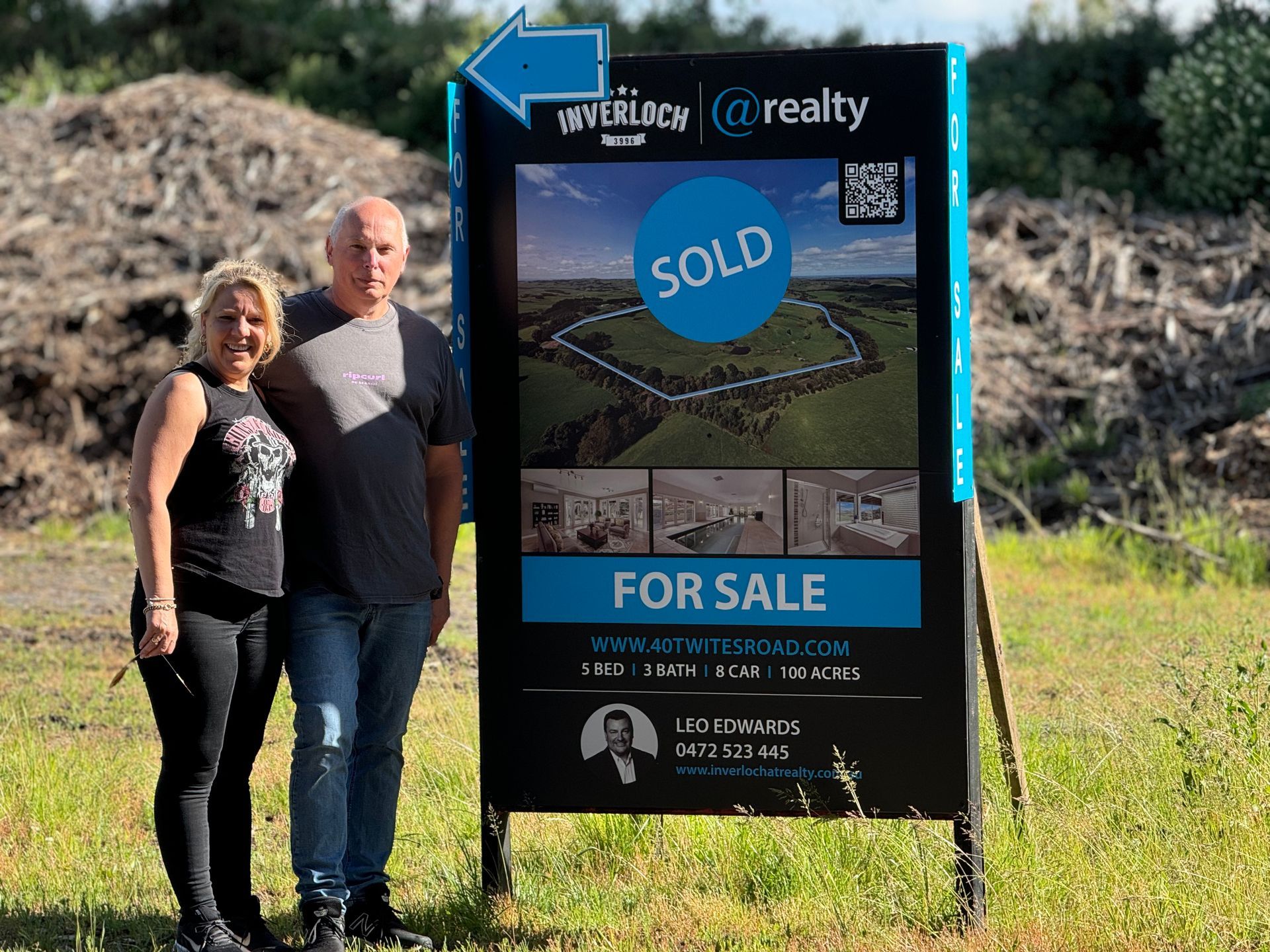 A man and a woman are standing in front of a sold for sale sign.