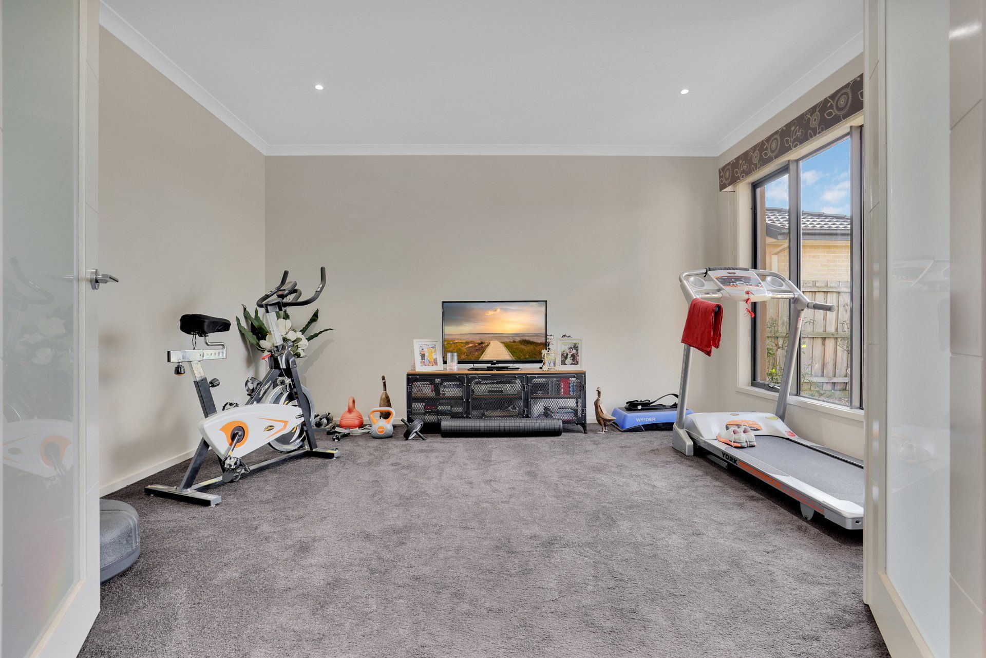 A living room with a treadmill , exercise bike , and television.