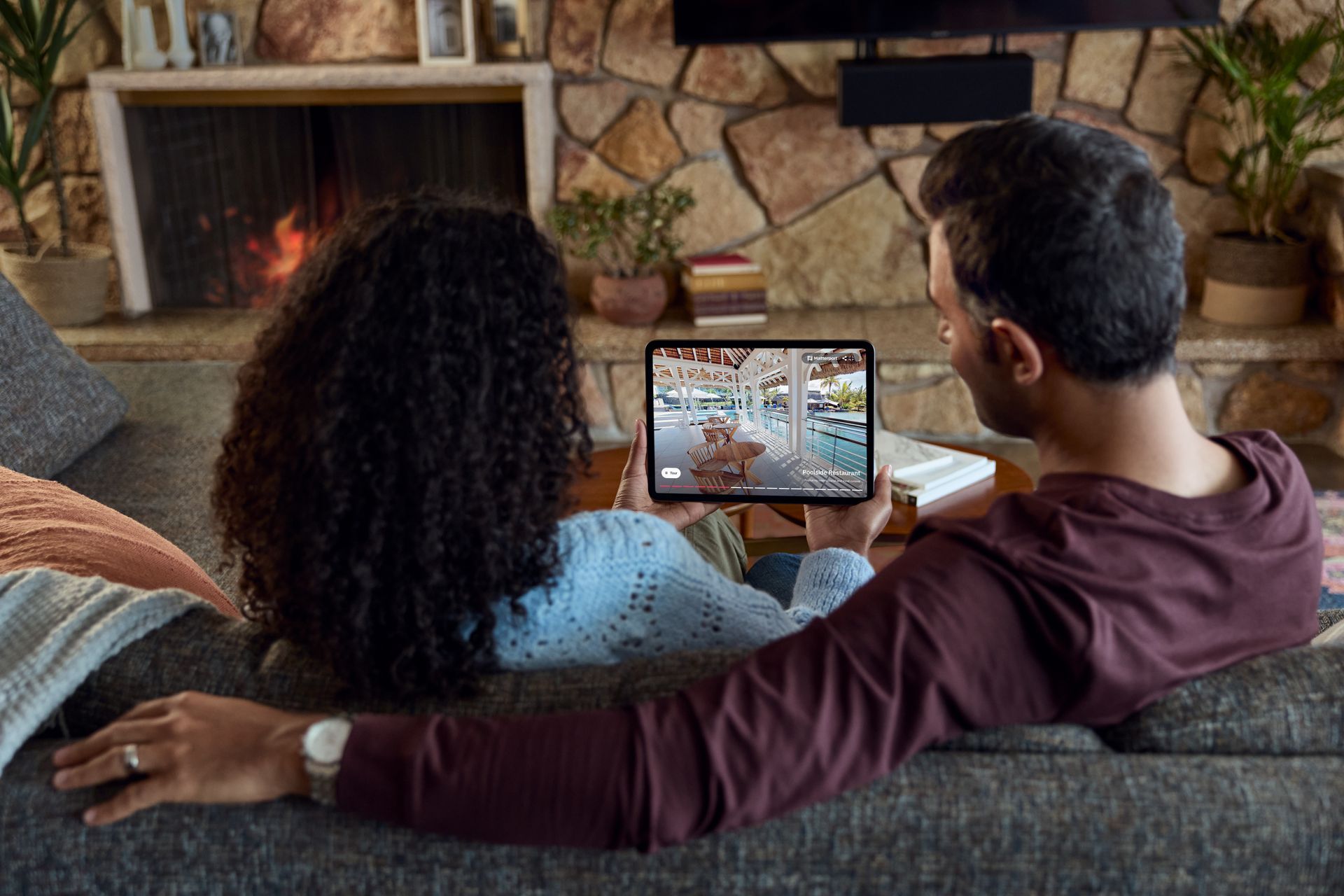 A man and a woman are sitting on a couch looking at a 3d tour on a tablet.