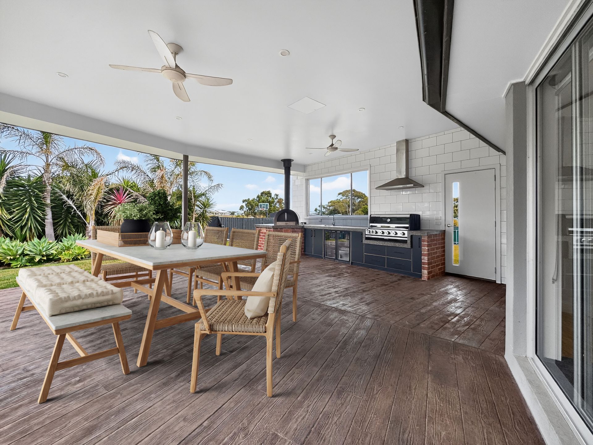 Outdoor kitchen and dining area with a wood-look floor, seating, and grill under a covered patio.