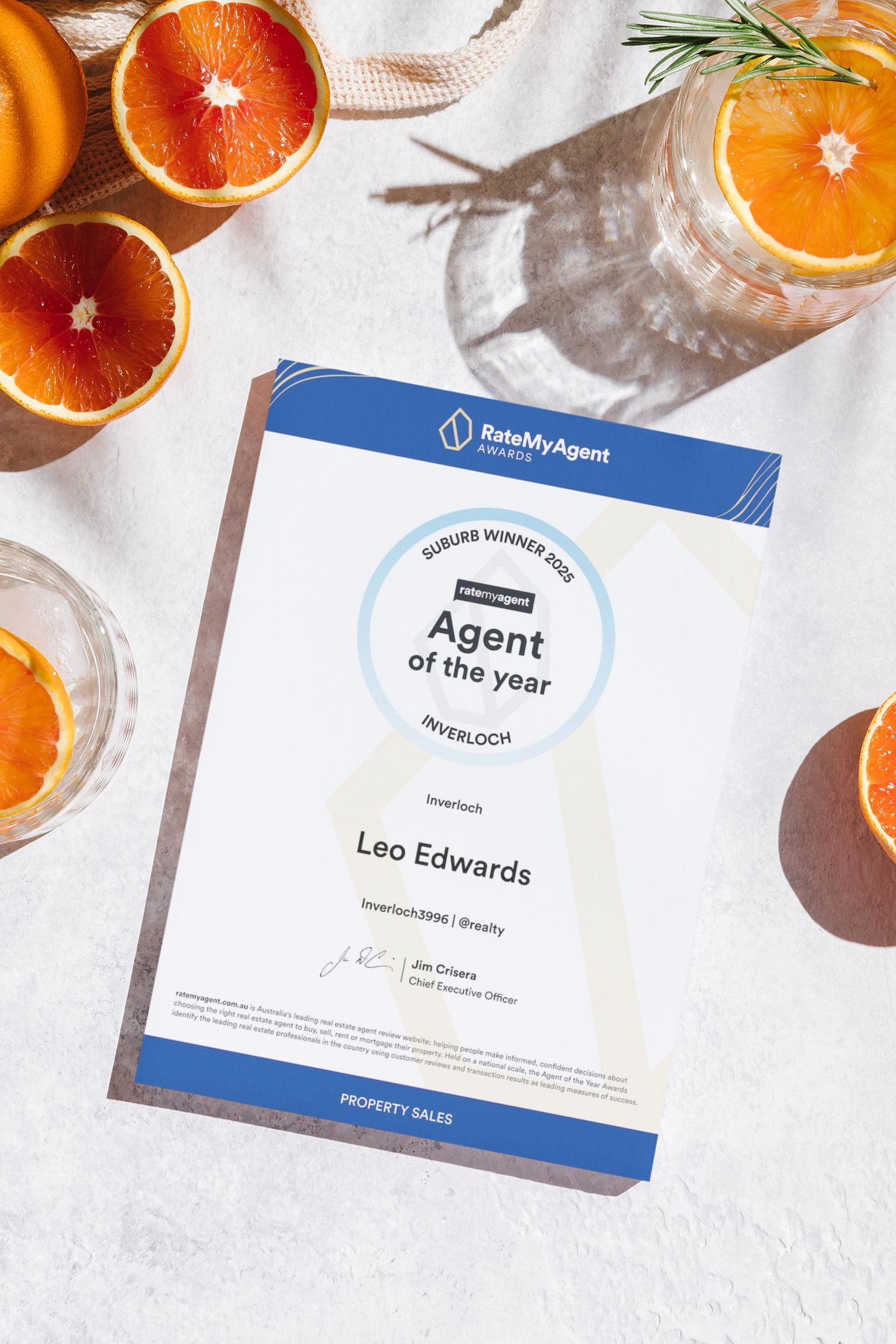 A certificate for an agent of the year Inverloch 2025 is sitting on a table next to oranges.