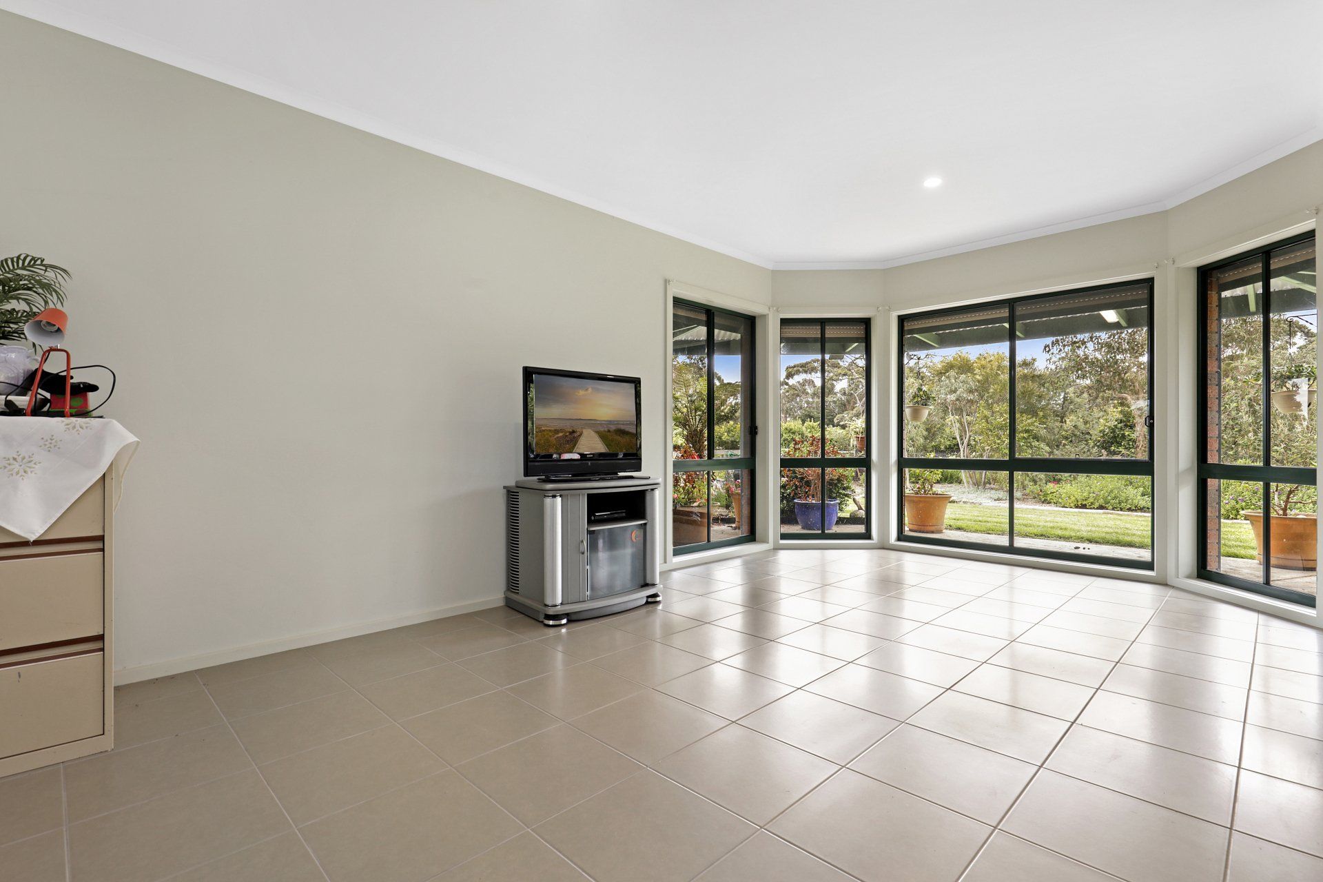 A living room with a television on a stand and lots of windows.