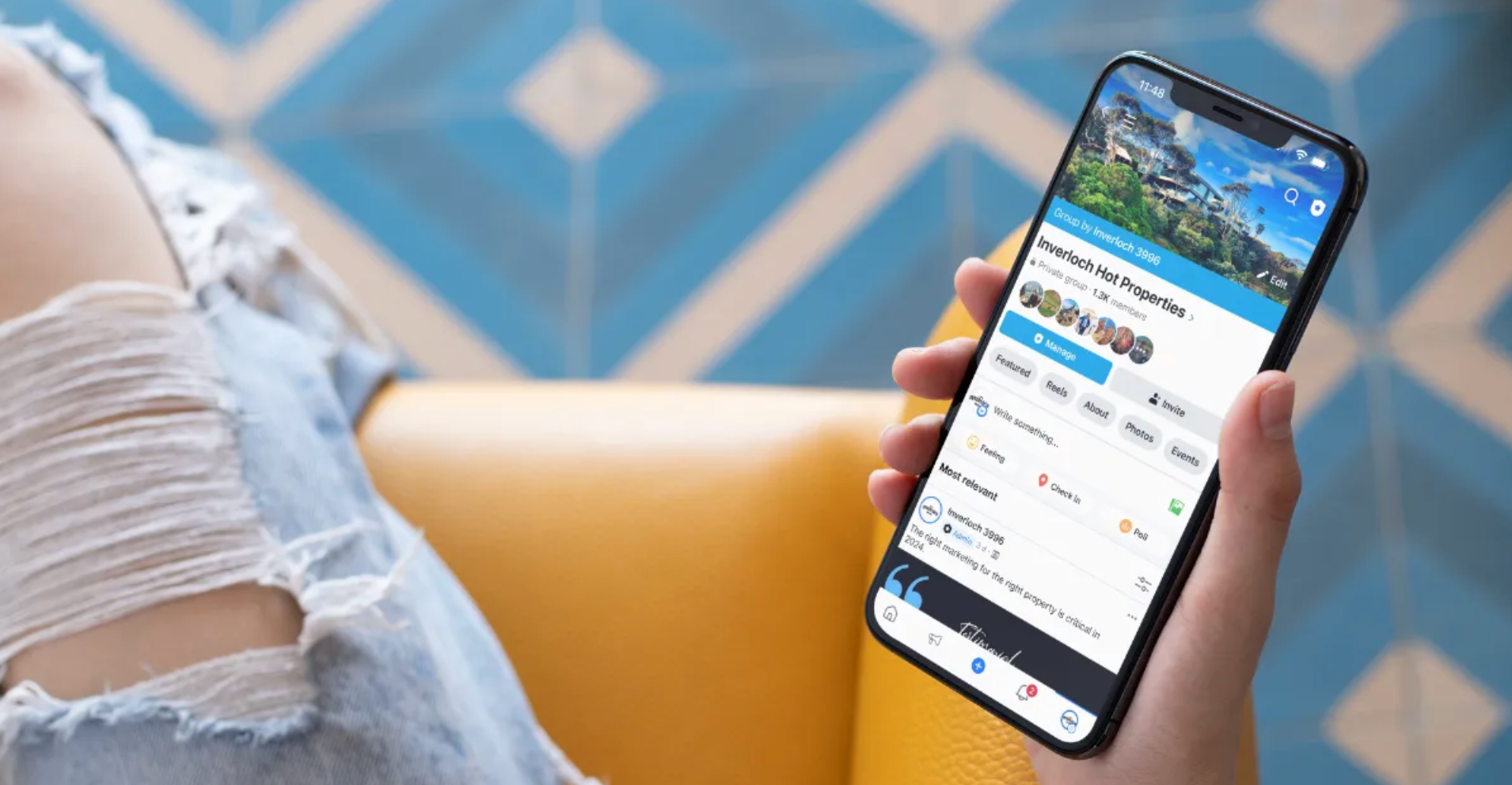 Person holding a phone displaying a travel website with a mountain image, sitting on a yellow chair.