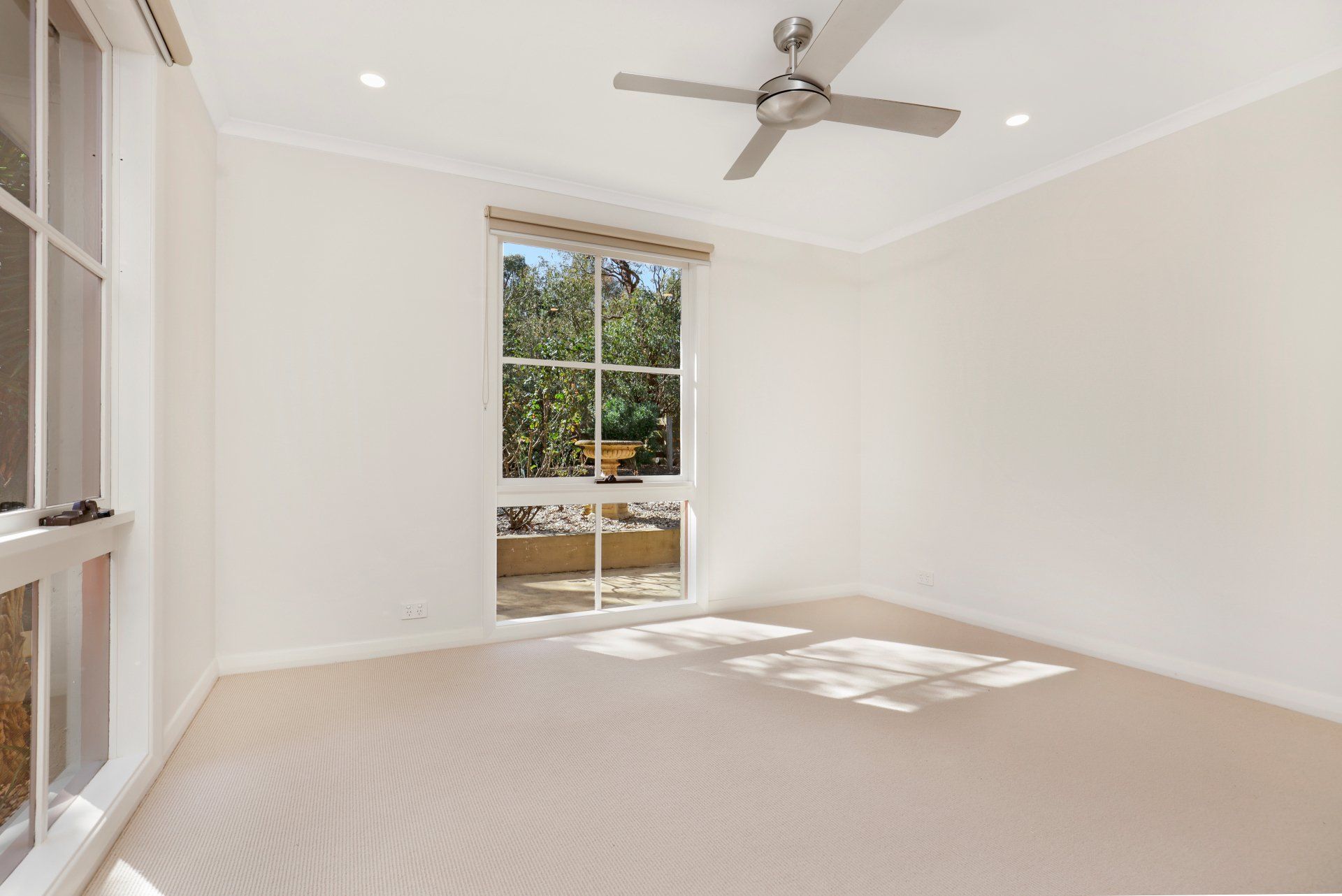 An empty room with a ceiling fan and a window.