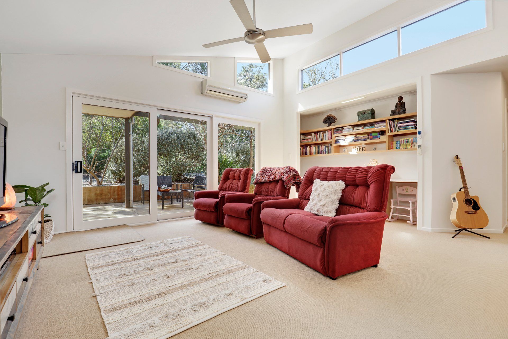 A living room with red couches , chairs , a guitar and a ceiling fan.