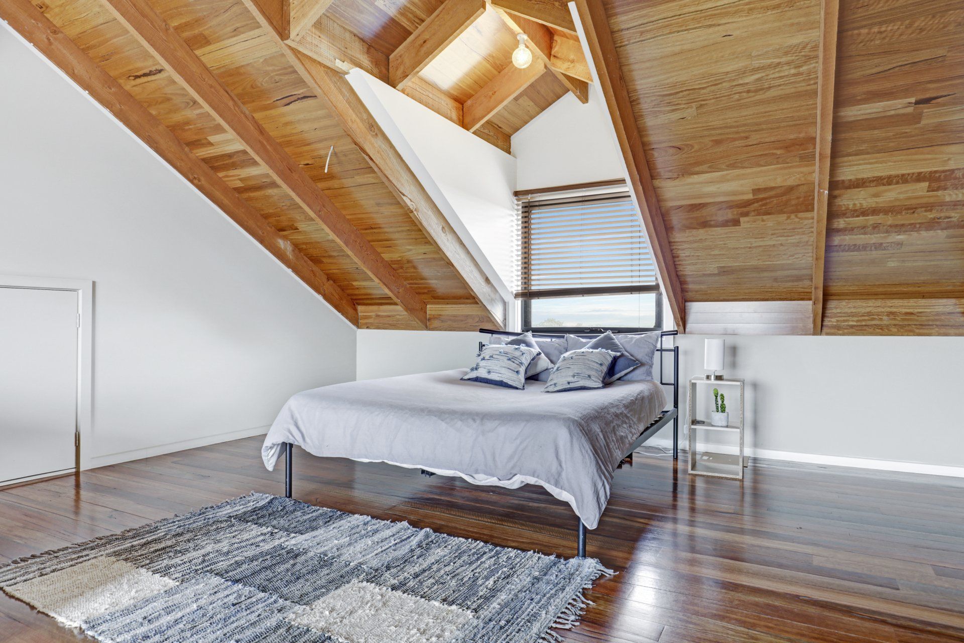 A bedroom with a bed , rug , and wooden ceiling.