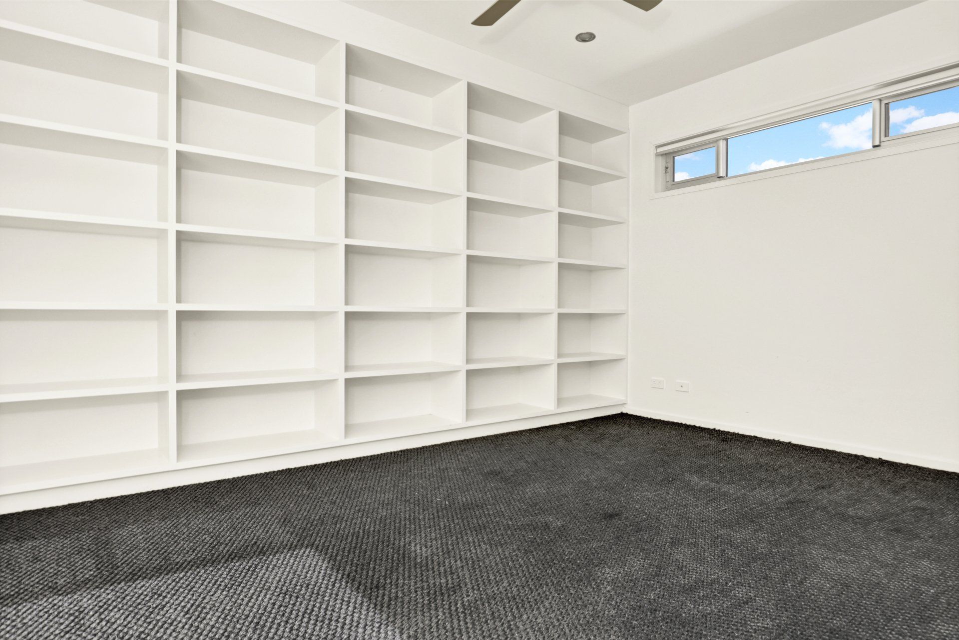 A room with a lot of shelves and a ceiling fan.