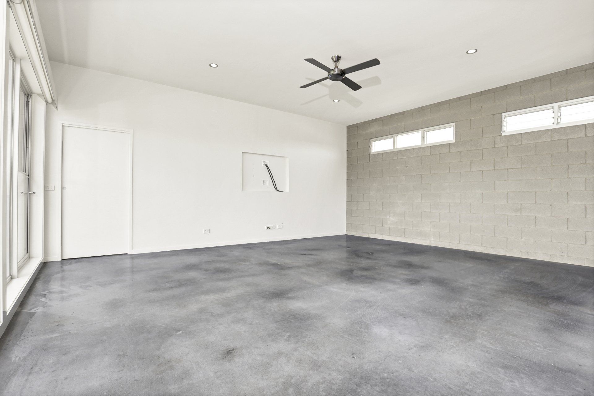 An empty room with a ceiling fan and a gray floor.
