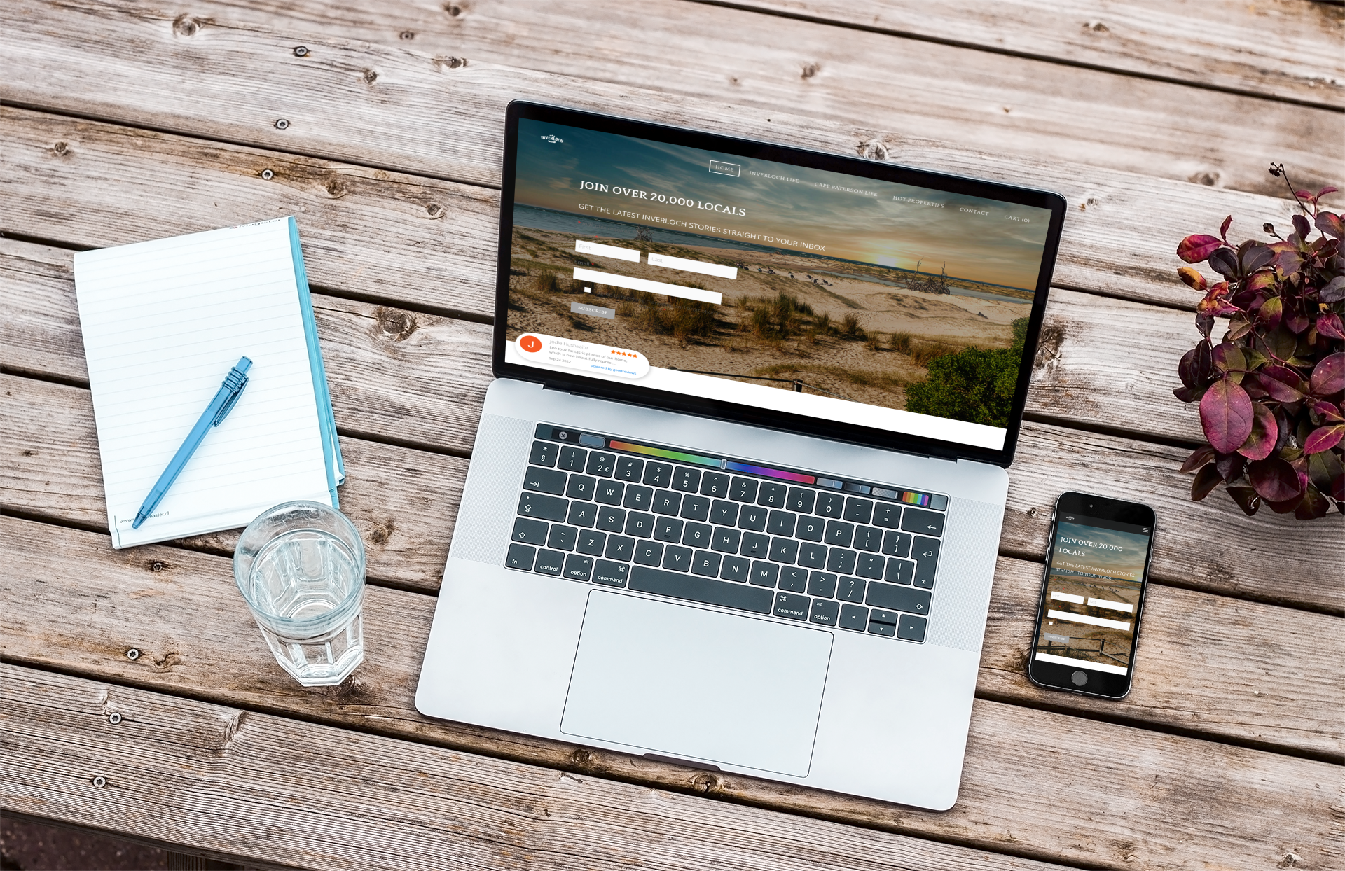 A laptop , cell phone , and notebook are on a wooden table.