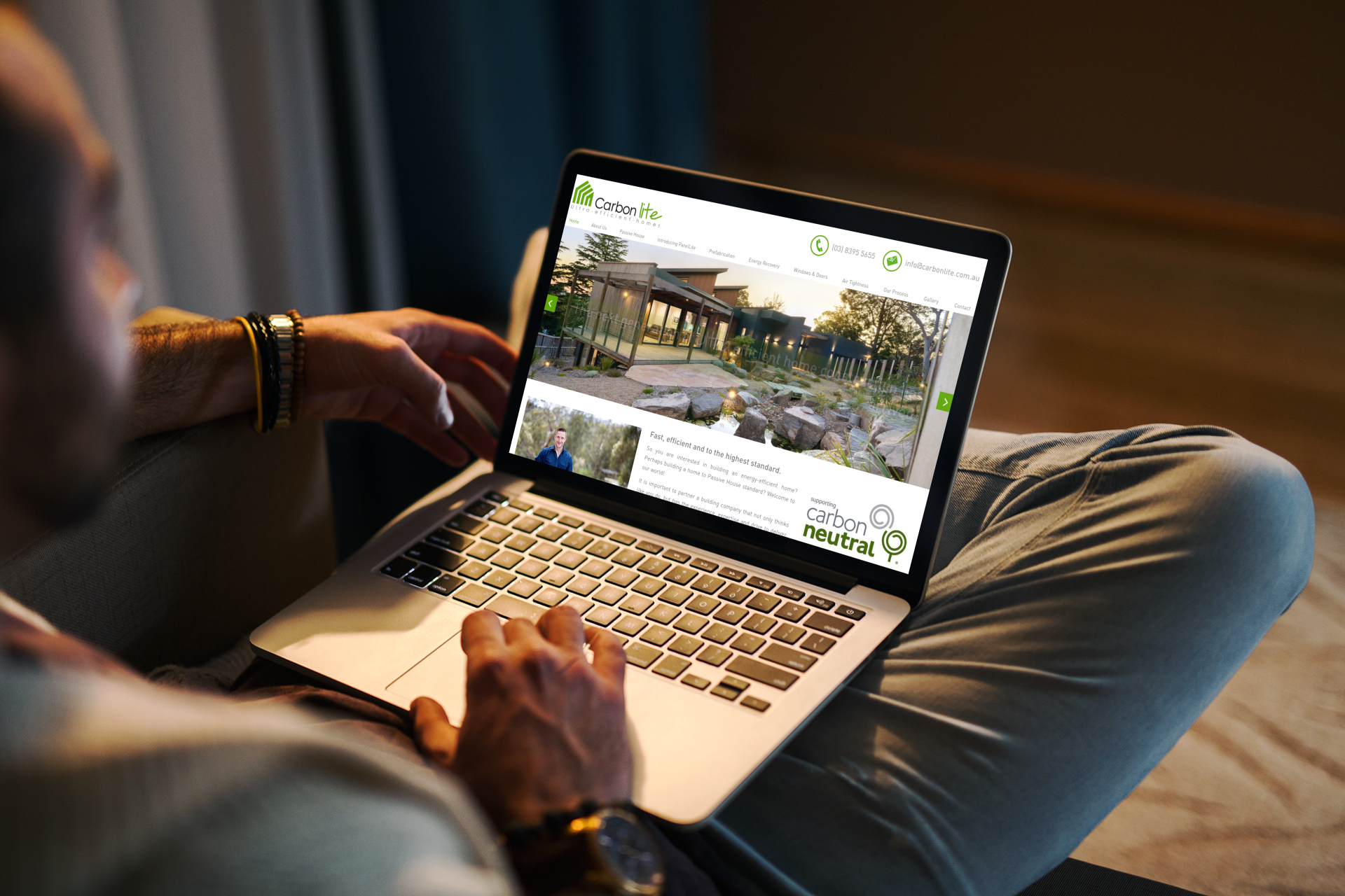 Man seated with a laptop, browsing a website featuring an outdoor structure, viewed from behind.