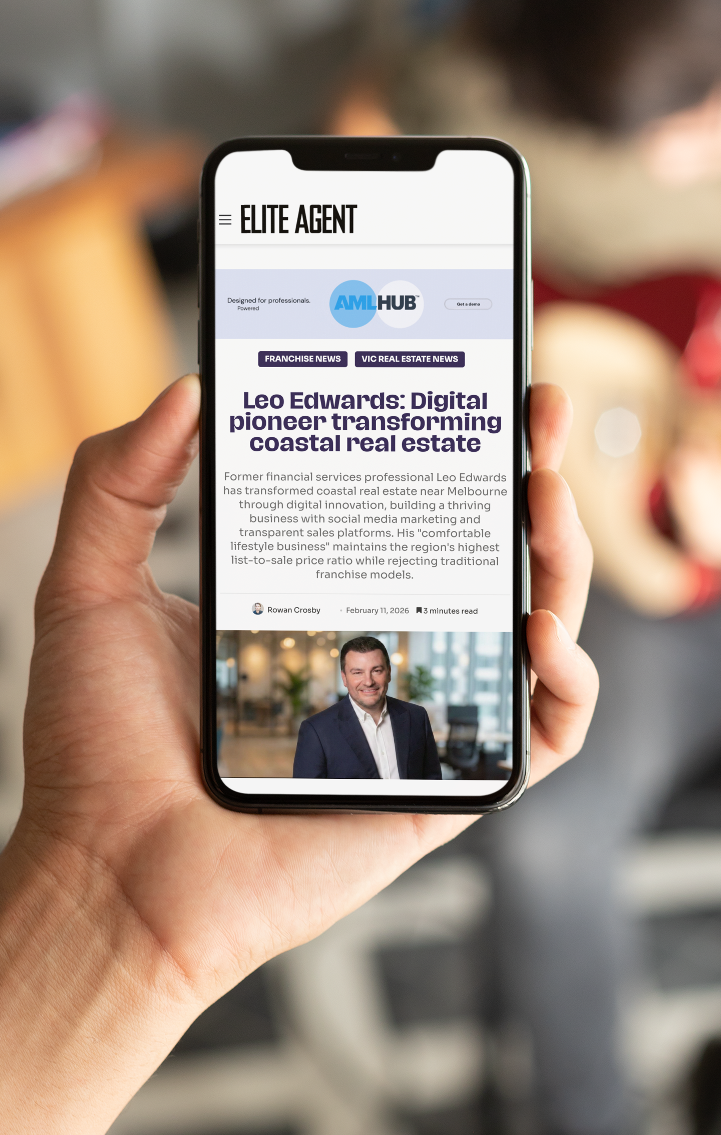 Hand holding smartphone displaying an article about coastal real estate, with a man's photo.