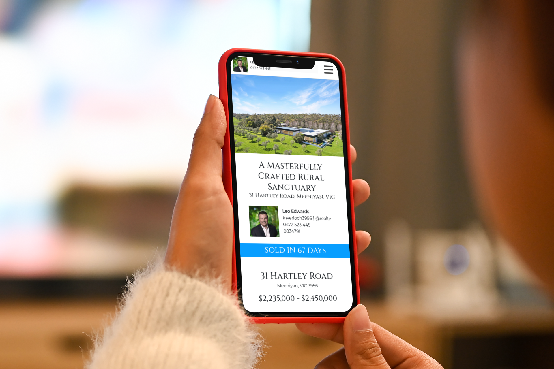 Hand holding a red smartphone showing a travel booking app with a scenic landscape image.