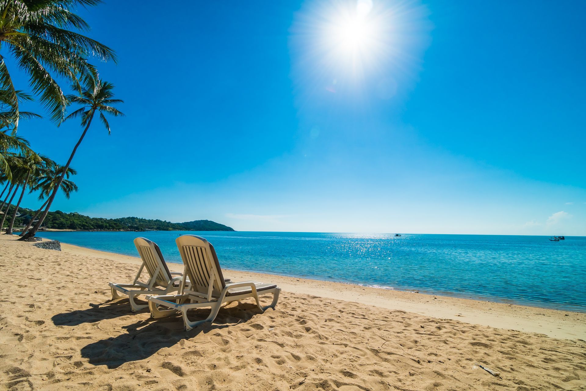 Two lounge chairs are sitting on a sandy beach next to the ocean.
