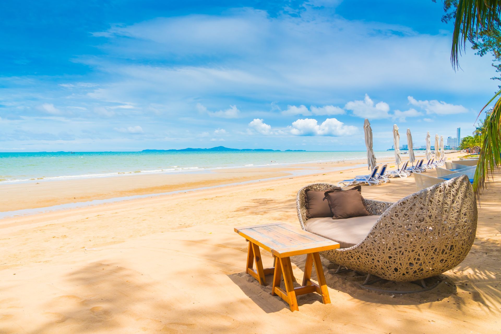 There is a wicker chair and a table on the beach.