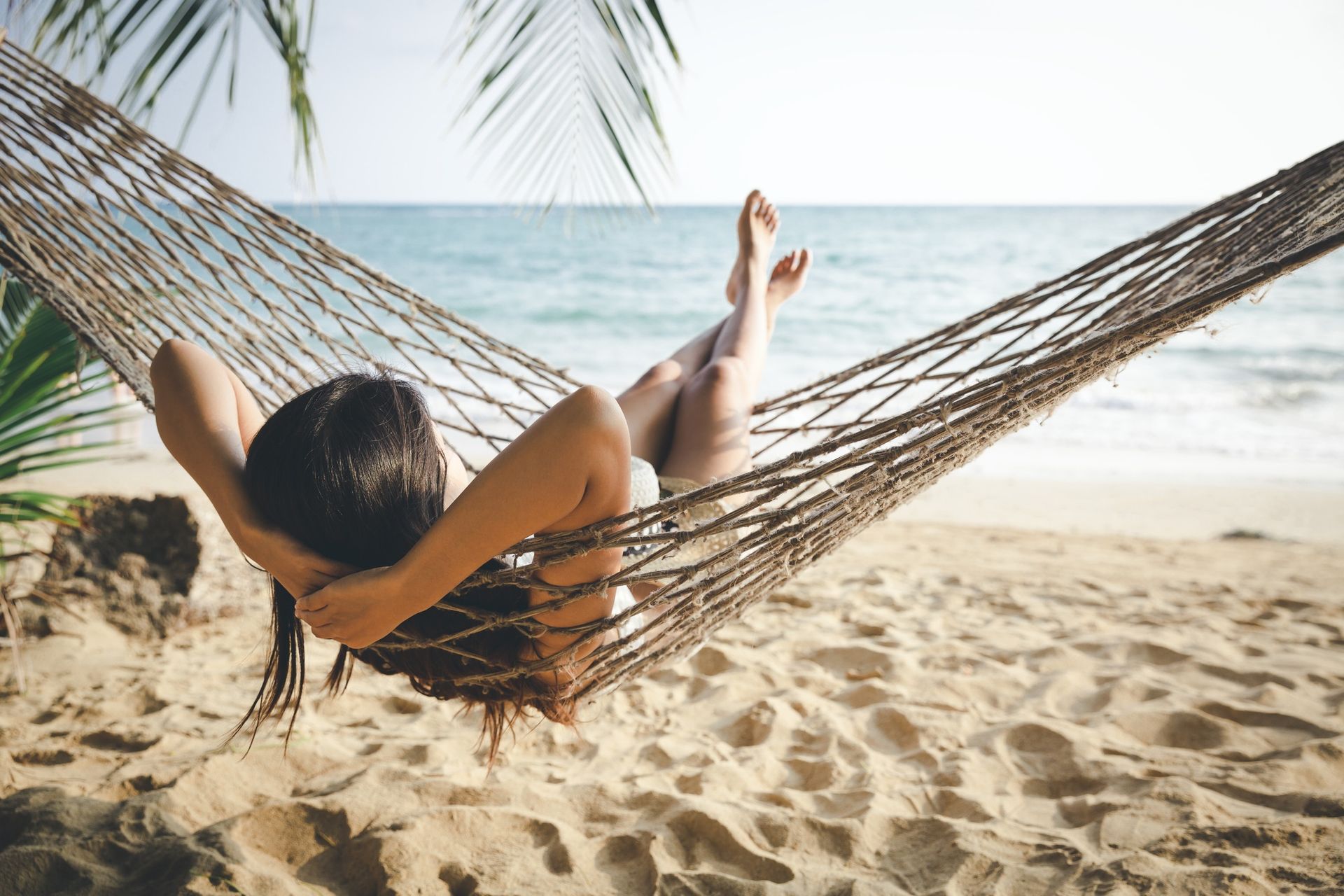 A woman is laying in a hammock on the beach.