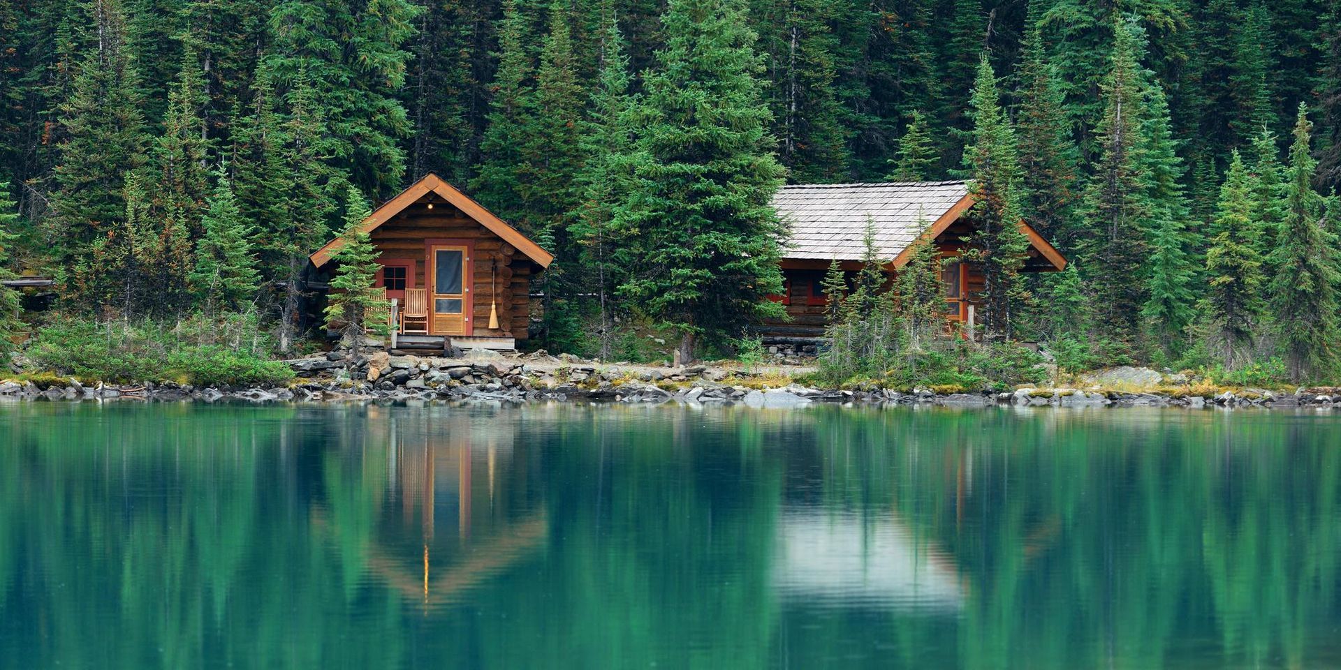 Two log cabins are sitting on the shore of a lake surrounded by trees.