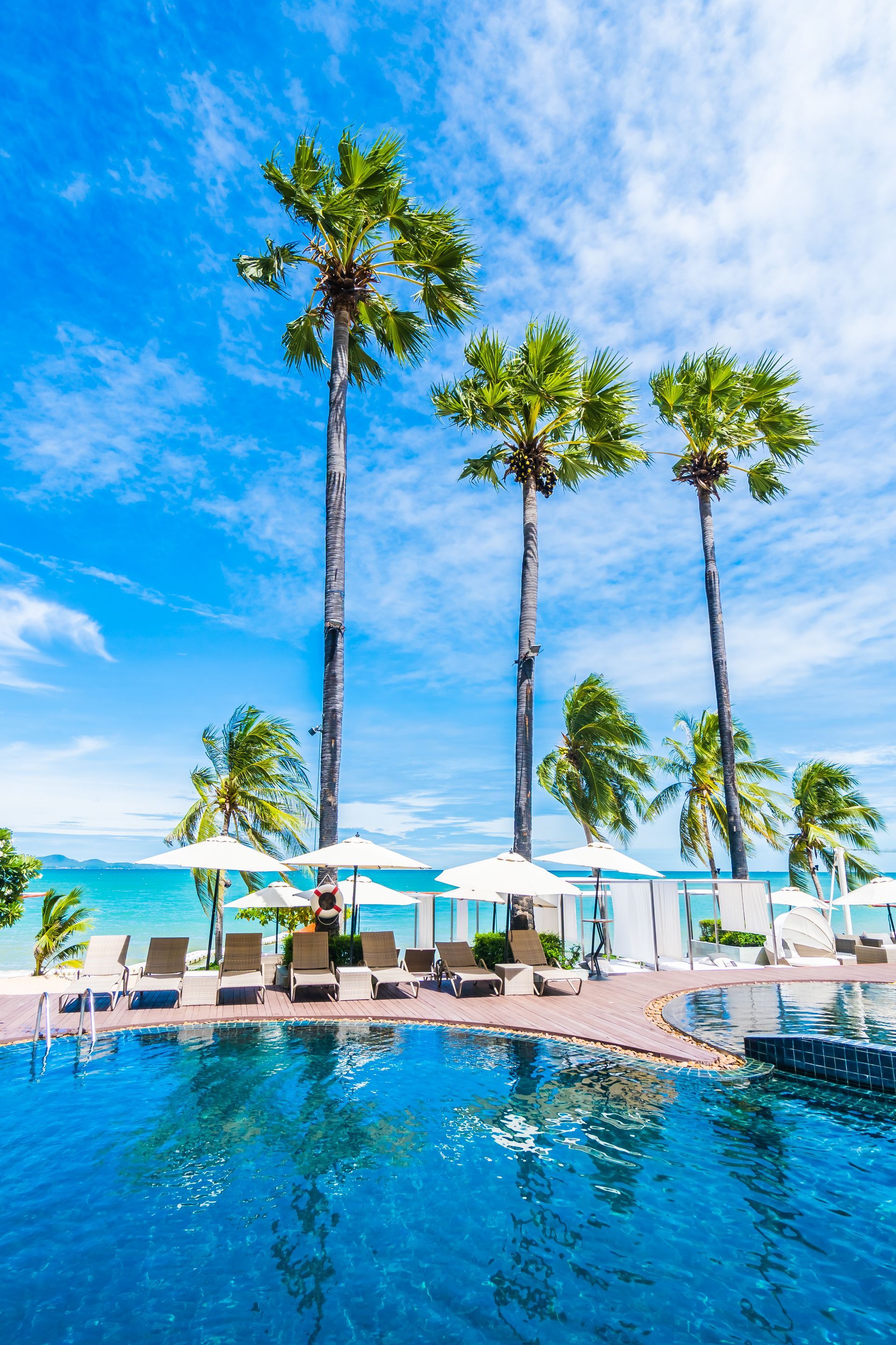 A swimming pool surrounded by palm trees and chairs on a tropical beach.