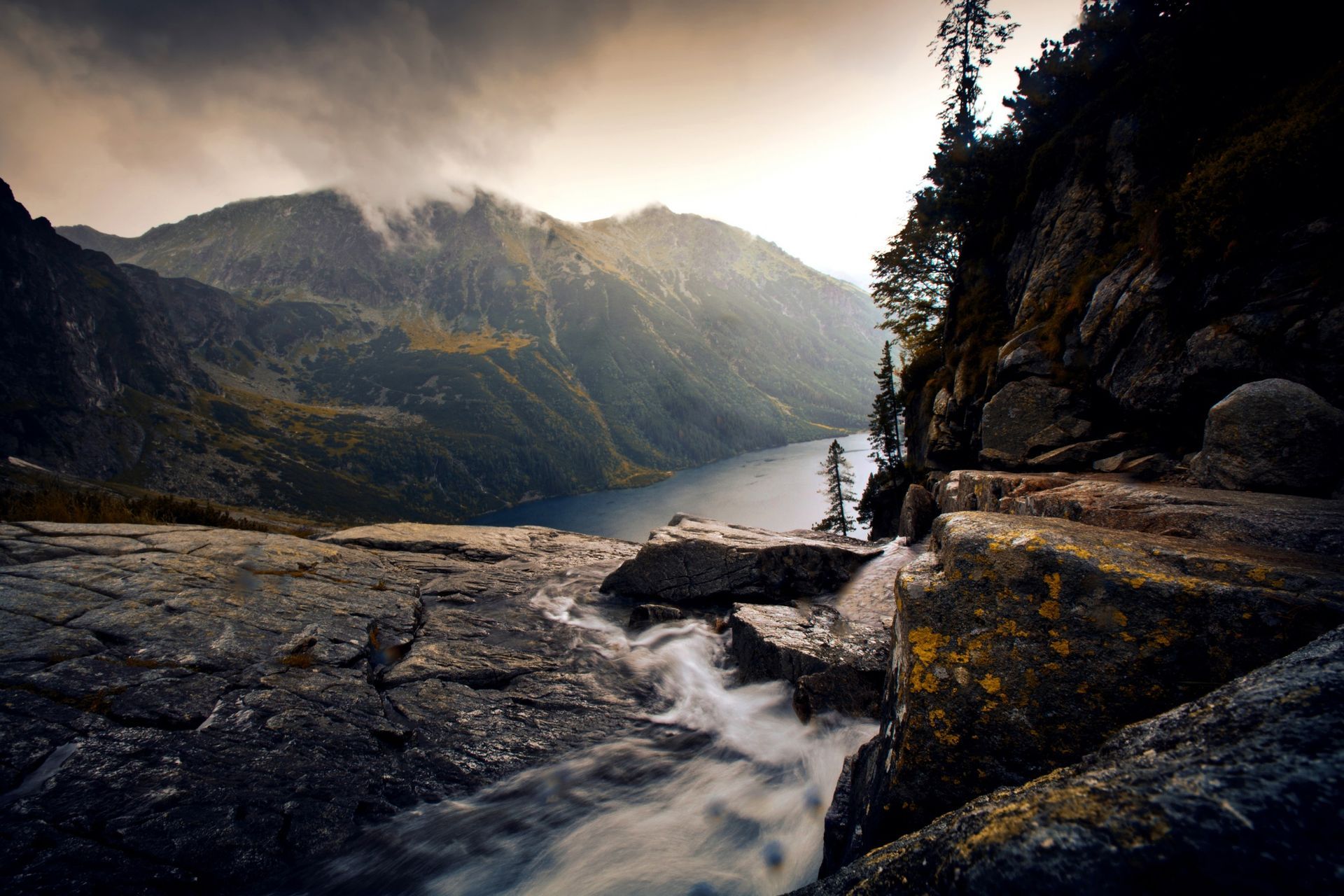 A river flowing down a rocky cliff into a lake surrounded by mountains.