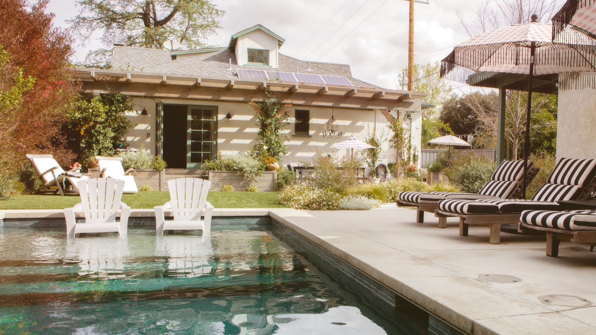 A swimming pool with chairs and umbrellas in front of a house