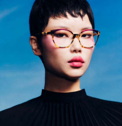 Portrait of a person in tortoiseshell glasses and black top against a blue background