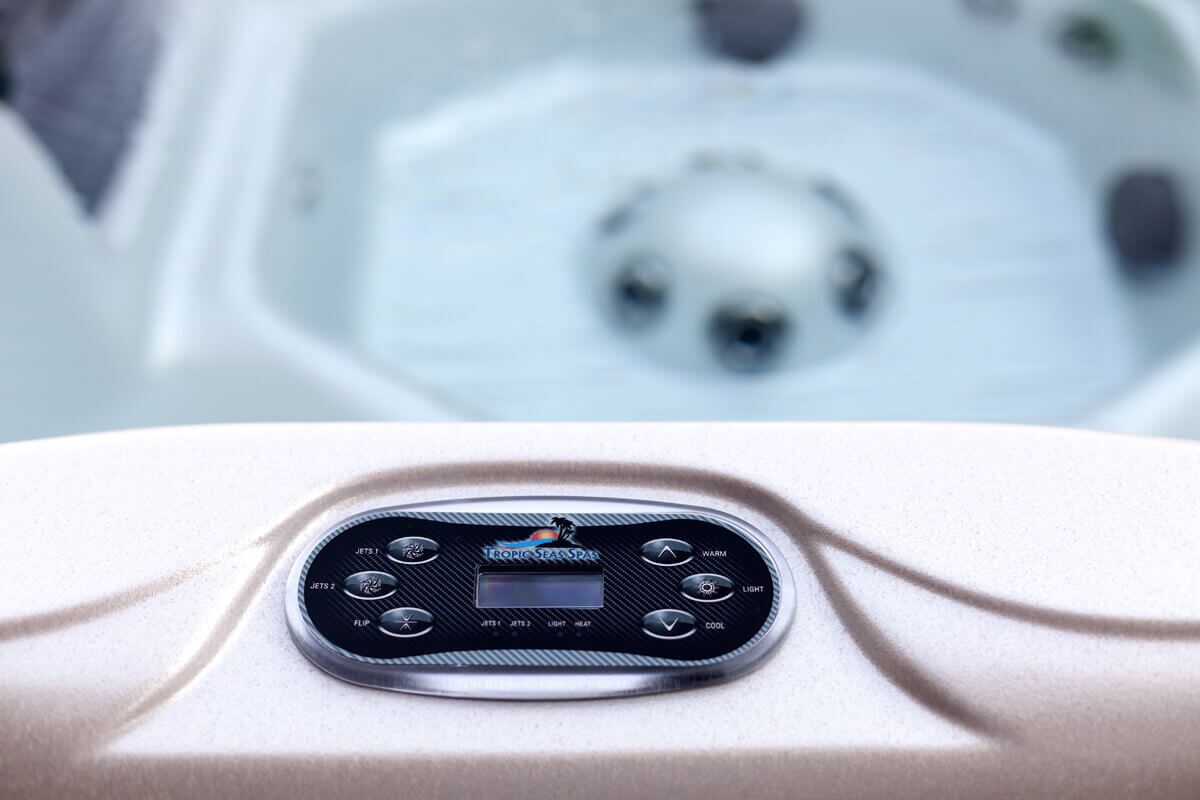 Close-up of a hot tub control panel with buttons and a digital display. The tub is filled with water. Hot tub control panel with buttons and display, set against a white hot tub interior.