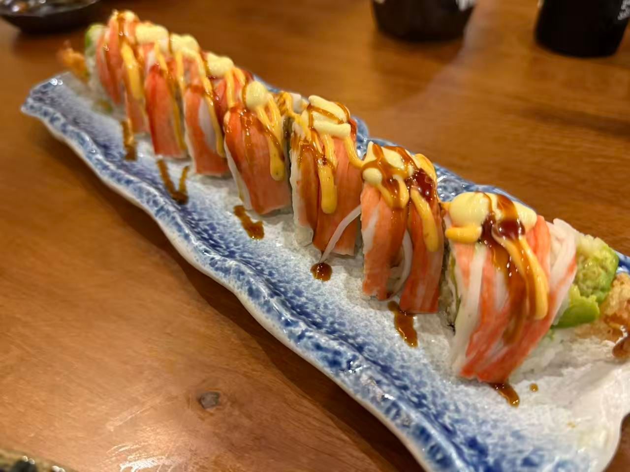 Sushi rolls drizzled with sauces on a long blue-rimmed plate on a wooden table
