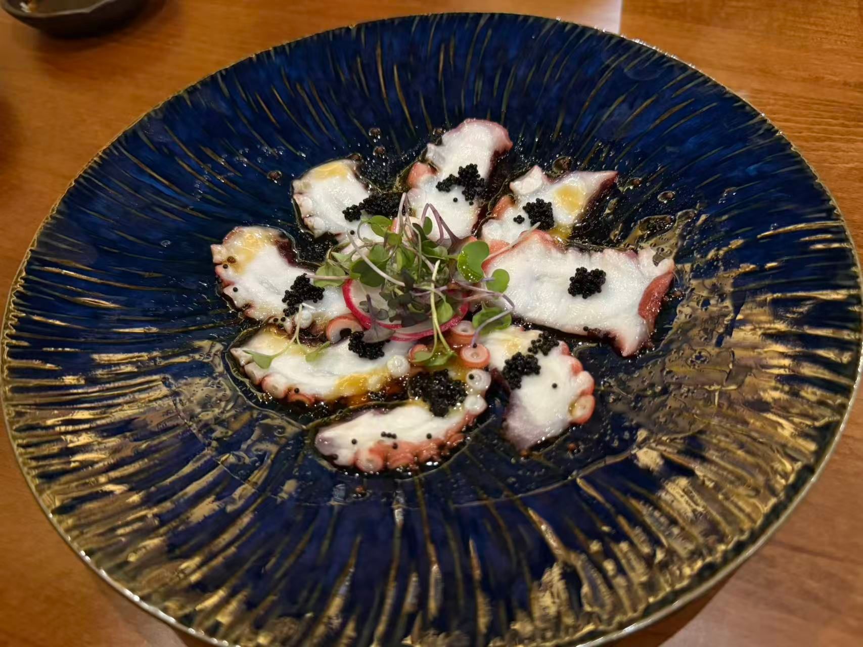 Sliced octopus on a dark blue plate, garnished with greens on a wooden table.