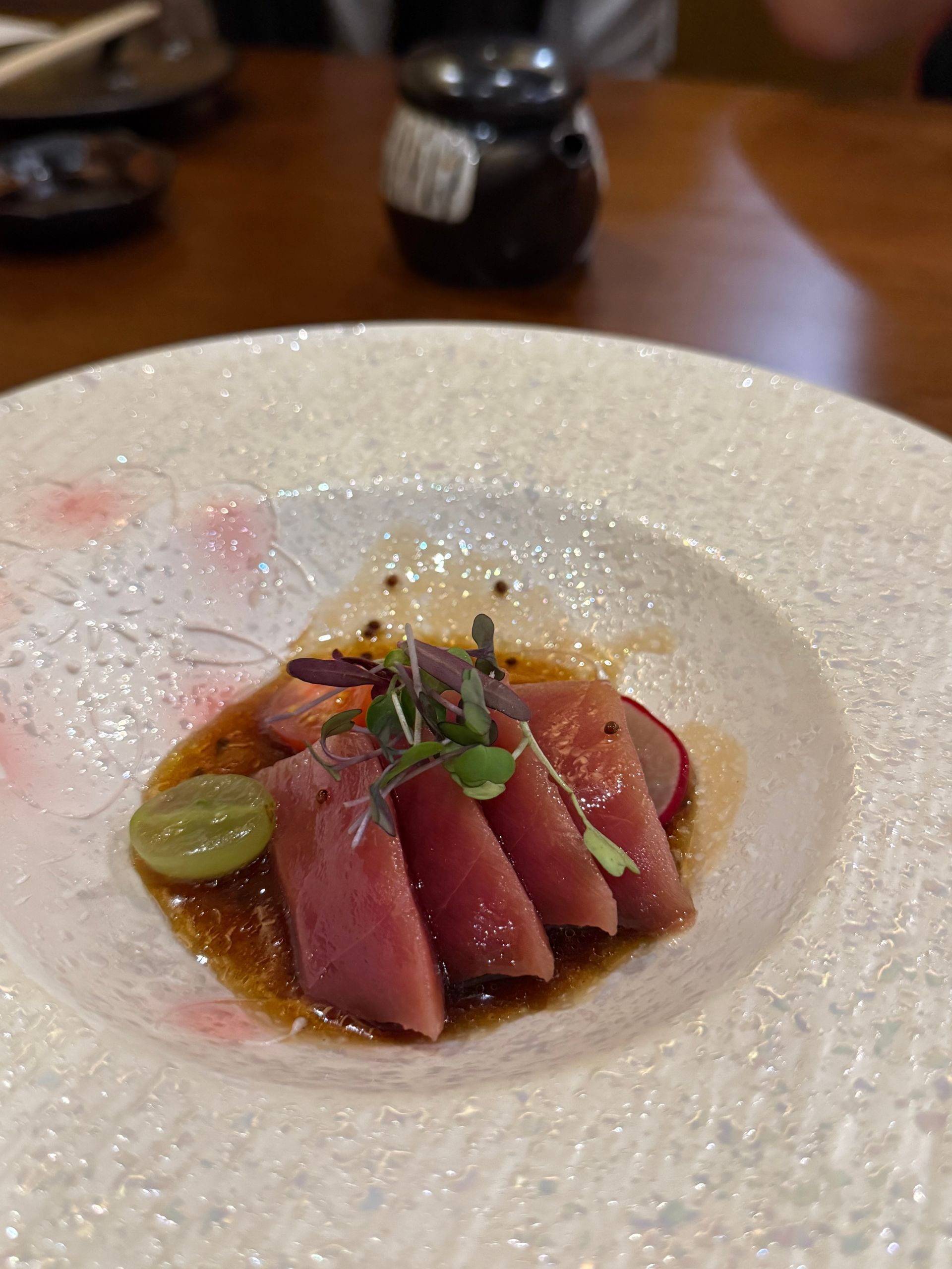 Plated seared tuna slices with garnish in a white bowl on a wooden table