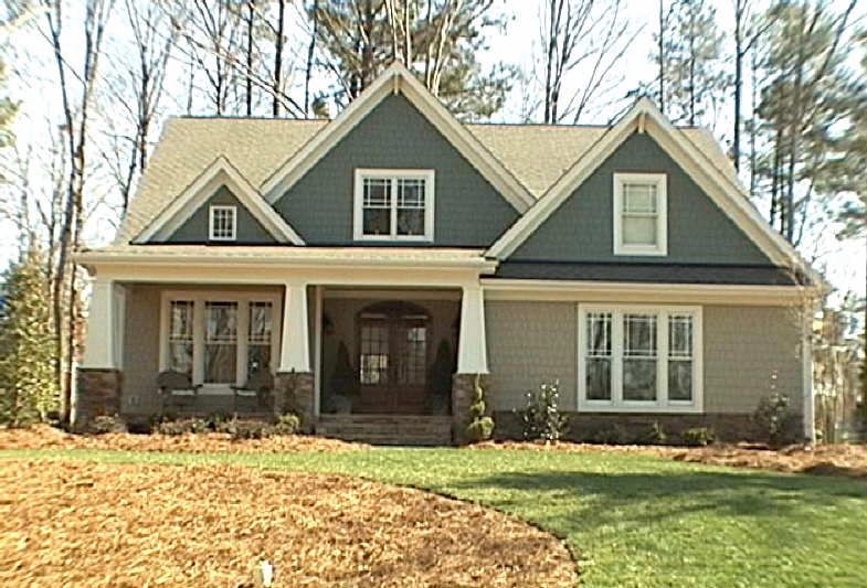 Sage green craftsman custom home with stone water table and covered front entry on a wooded lot in Holly Springs NC