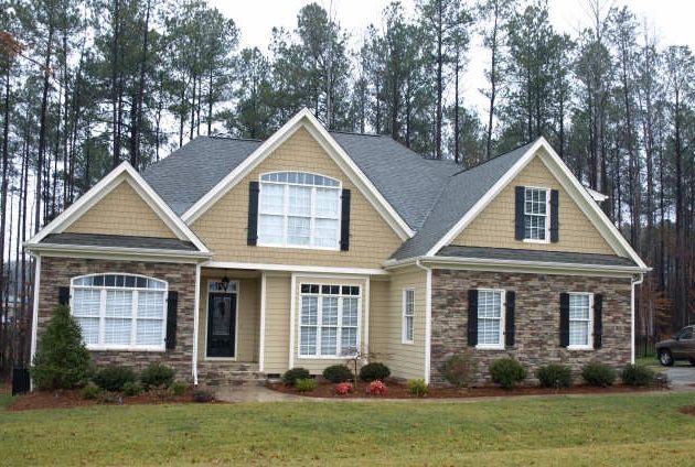 Custom craftsman home with tan siding and stone foundation built on a wooded lot in Holly Springs NC