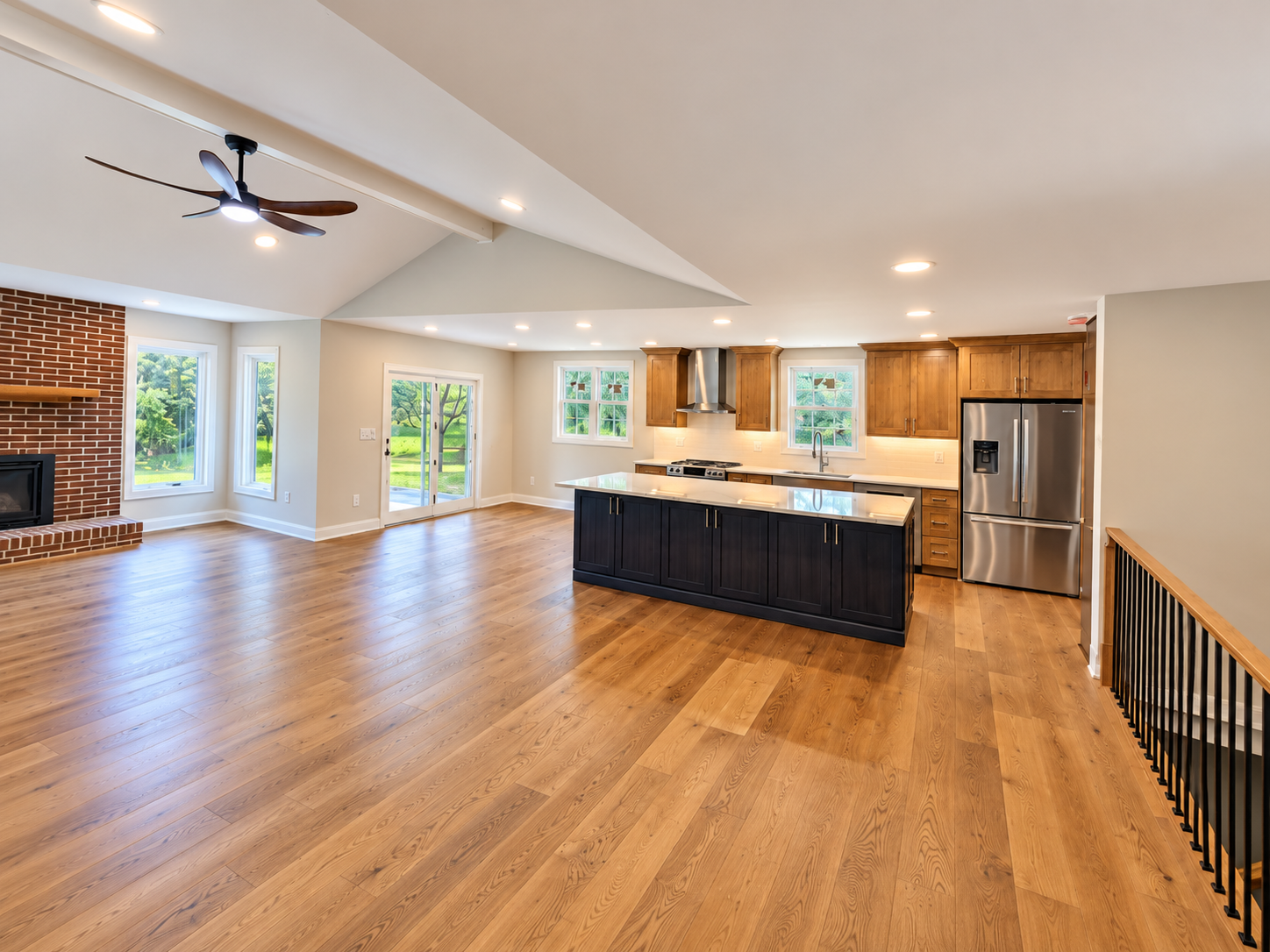 Spacious open-plan kitchen and living room with wood floors, island, large windows, and ceiling fan.