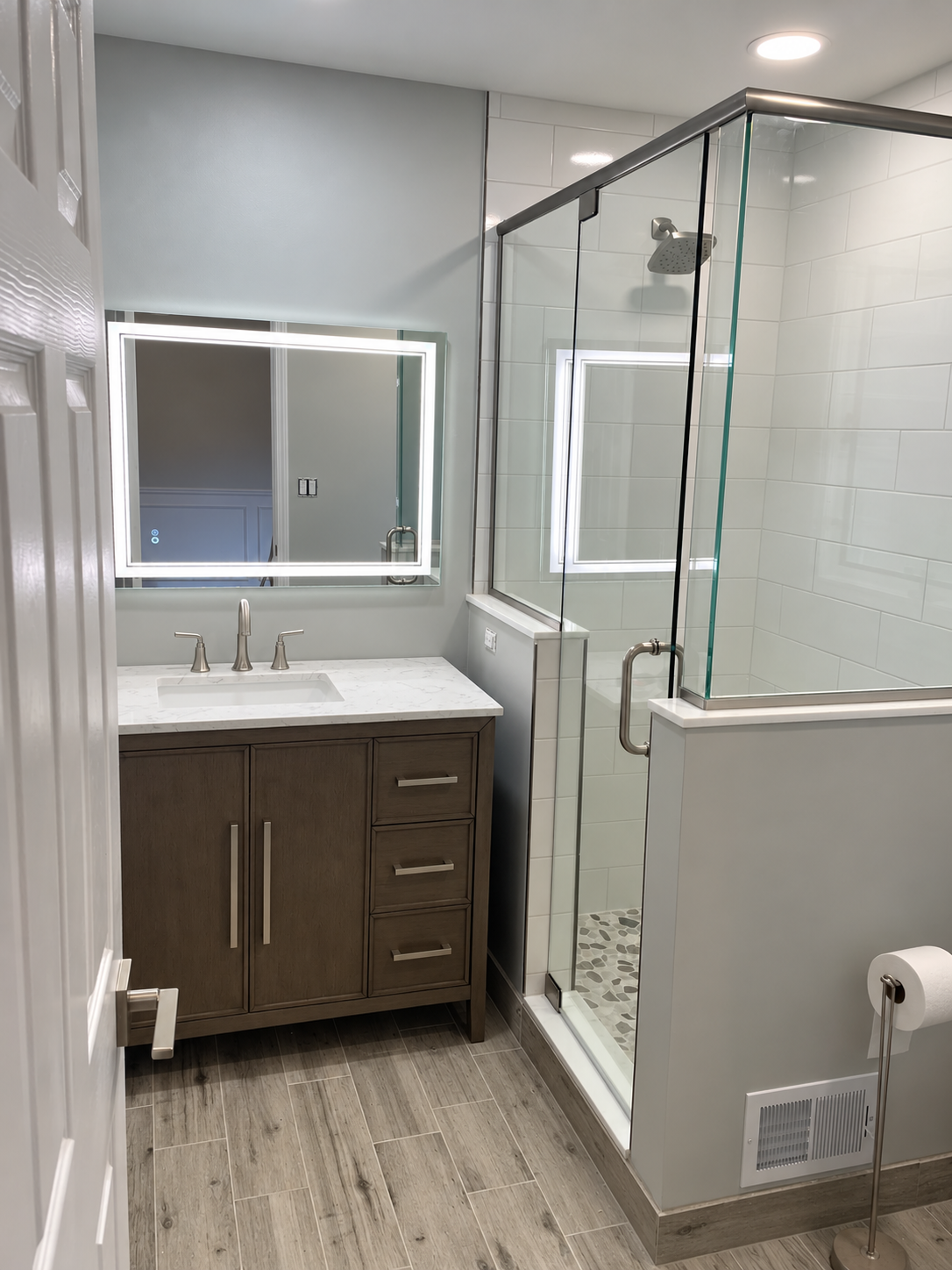 Modern bathroom with shower, vanity, mirror, and glass partition on a tiled floor.
