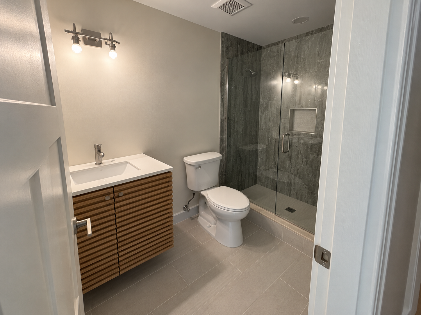 Modern bathroom with sink vanity, toilet, and glass shower enclosure in gray tones