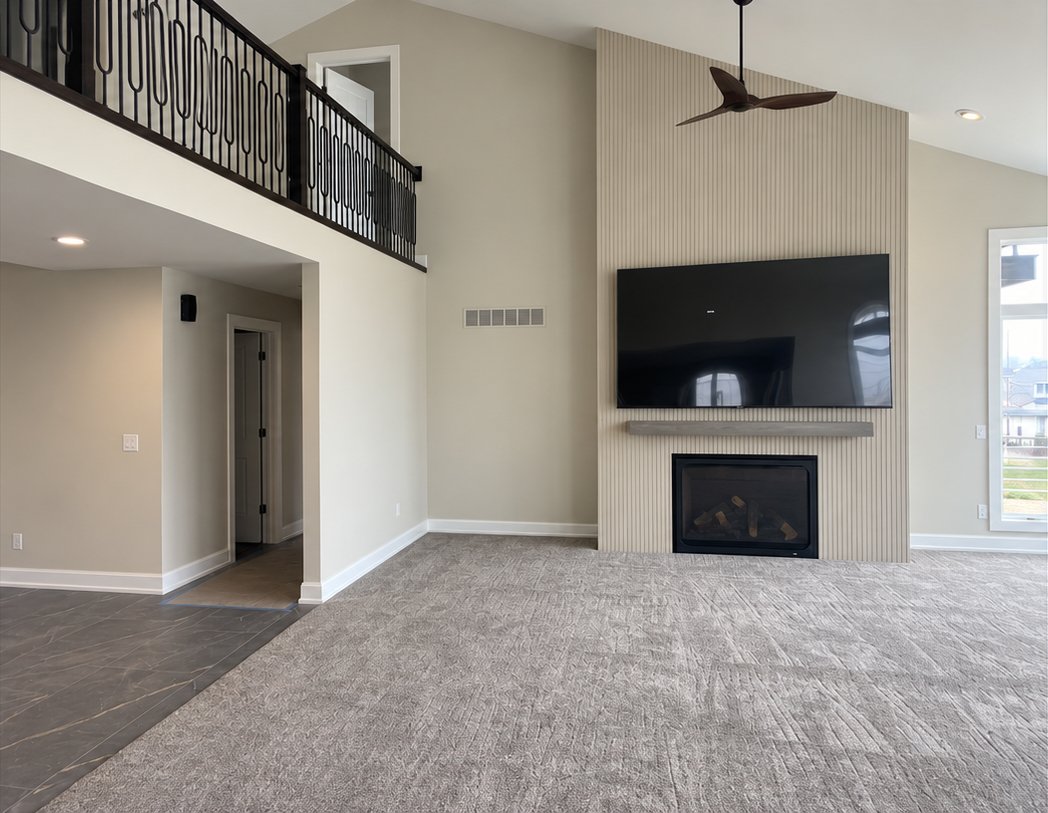 Empty living room with gray carpet, fireplace, and wall-mounted TV beneath a ceiling fan