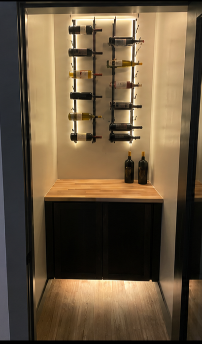 Small wine storage alcove with wall-mounted racks, a countertop, and two bottles on display.