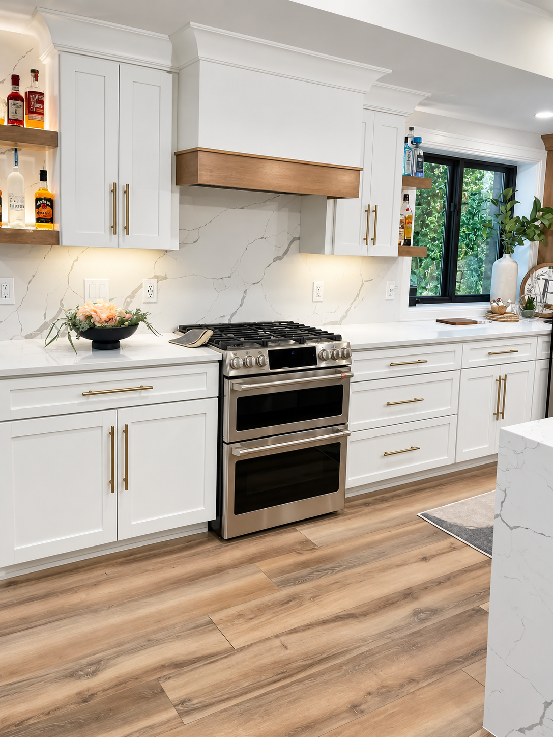 Bright white kitchen with stainless steel stove, cabinets, island, and wood-look flooring.