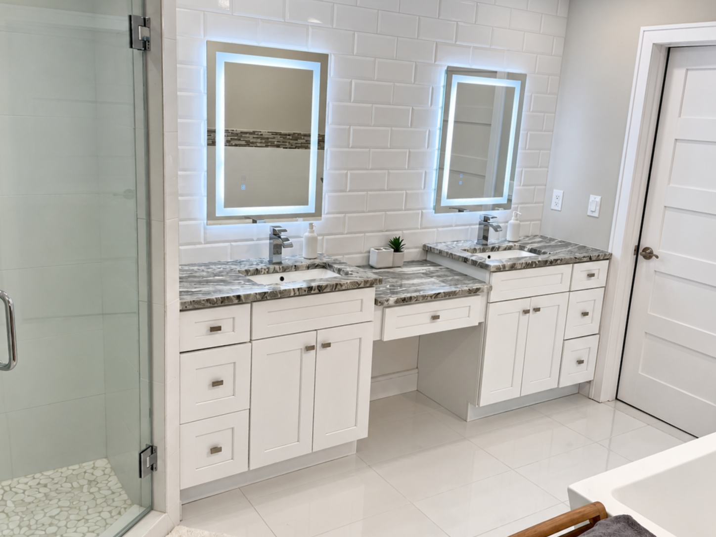 Modern bathroom with double vanity, illuminated mirrors, glass shower, and white tile walls