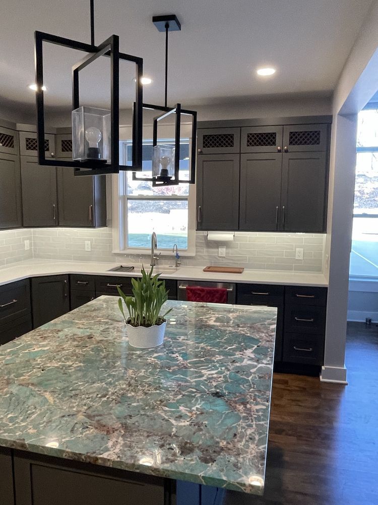 Modern kitchen with dark cabinets, white backsplash, and a marbled island beneath pendant lights