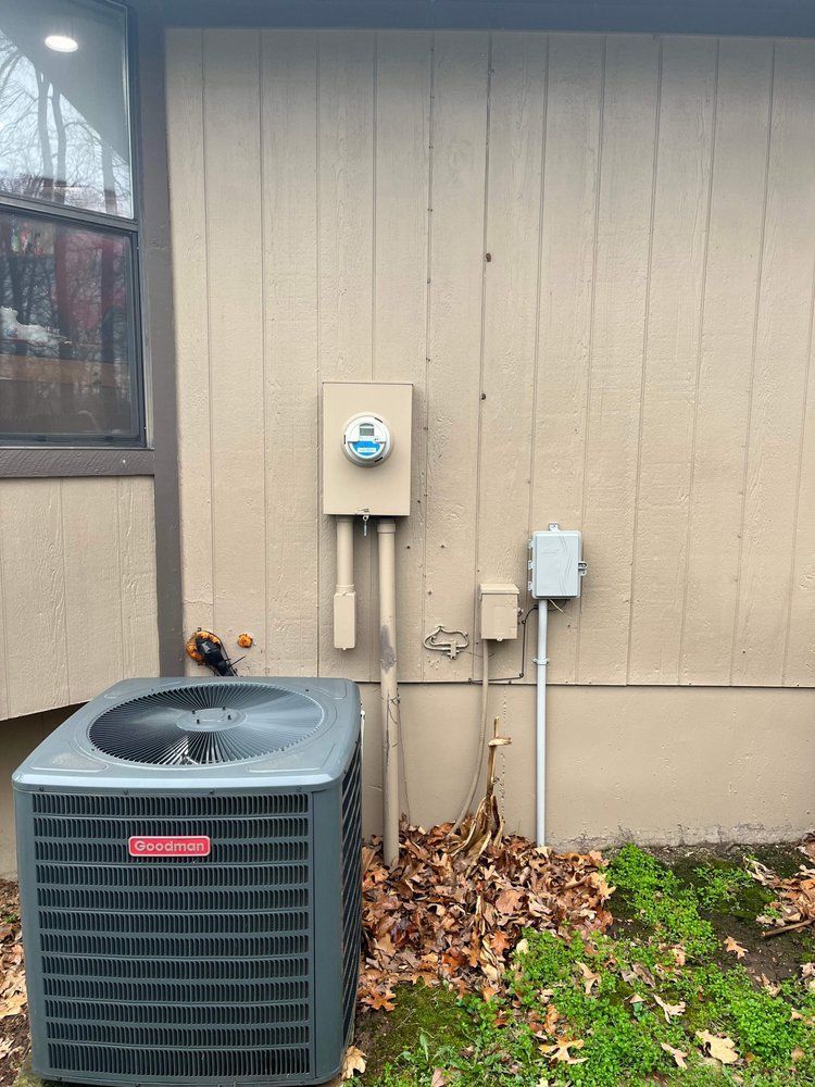 Air conditioning unit next to a building with a power meter and electrical boxes on a beige wall.