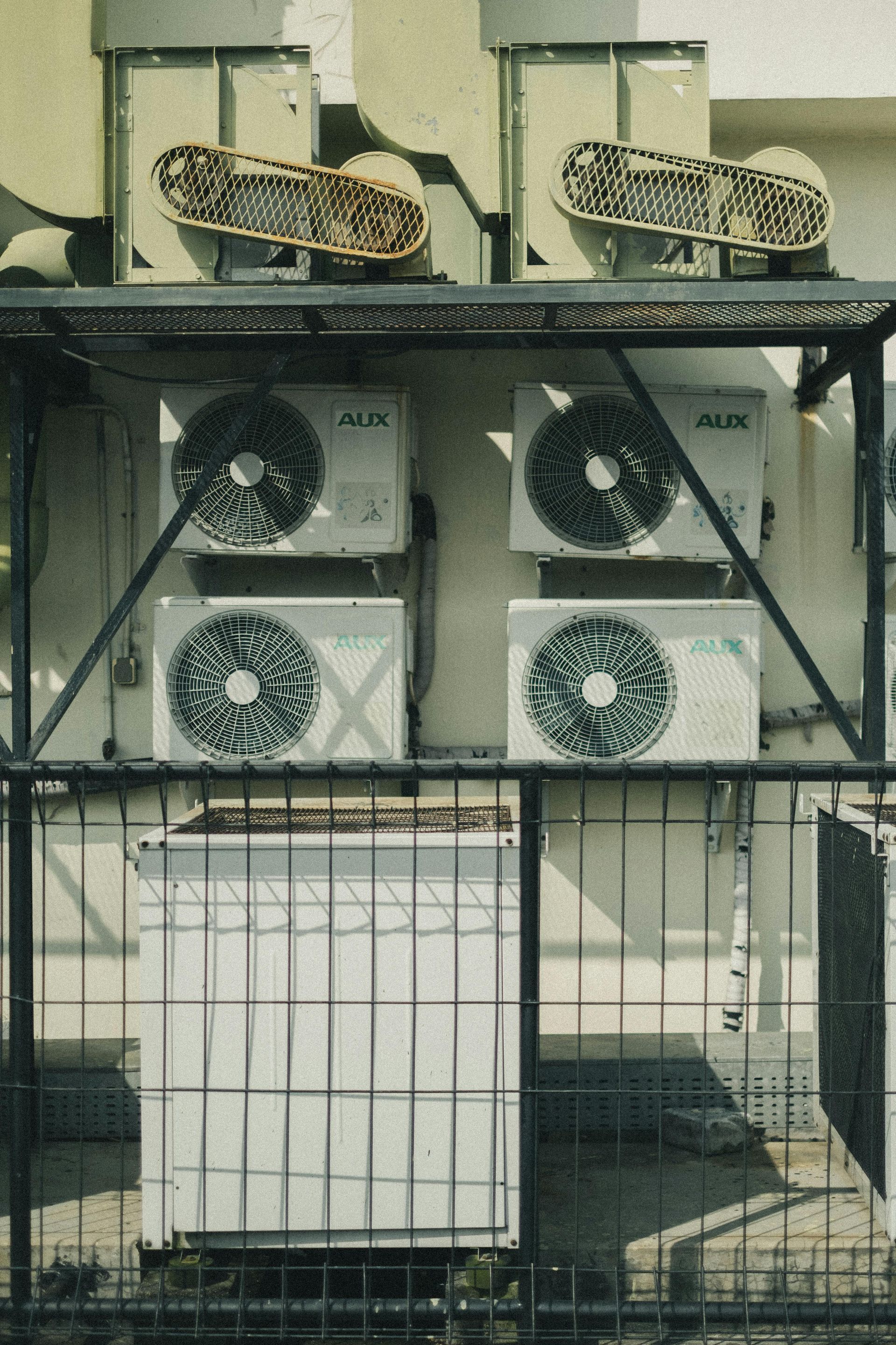 Air conditioning units mounted on a building, with a metal cage around them.